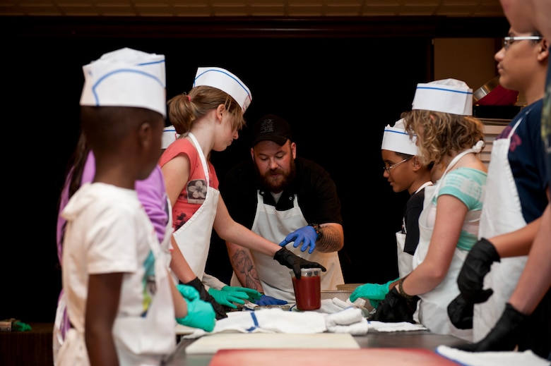 PETERSON AIR FORCE BASE, Colo. –Kirk Dunning, Club sous chef, teaches kids how to make homemade barbeque sauce during the Kids Barbecue Cooking Camp at The Club, Jan. 17, 2015. The kids learned barbecue and grill techniques along with how to prepare a full meal including chicken kabobs, tilapia, homemade barbecue sauce, salad and a desert. (U.S. Air Force photo by Senior Airman Tiffany DeNault)
