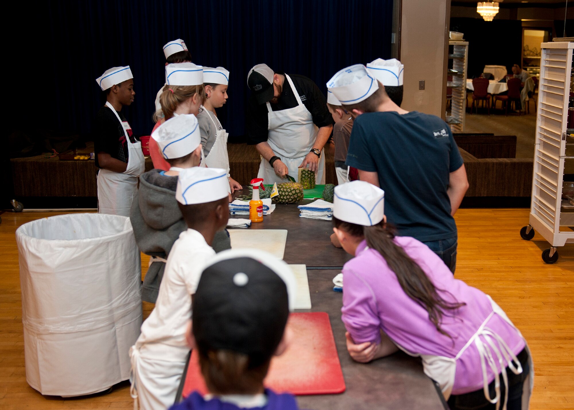 PETERSON AIR FORCE BASE, Colo. –Joe Zamora, Club executive chef, teaches kids how to properly cut a pineapple during the Kids Barbeque Cooking Camp at The Club, Jan. 17, 2015. The kids learned barbecue and grill techniques along with how to prepare a full meal including chicken kabobs, tilapia, homemade barbecue sauce, salad and a desert. (U.S. Air Force photo by Senior Airman Tiffany DeNault)