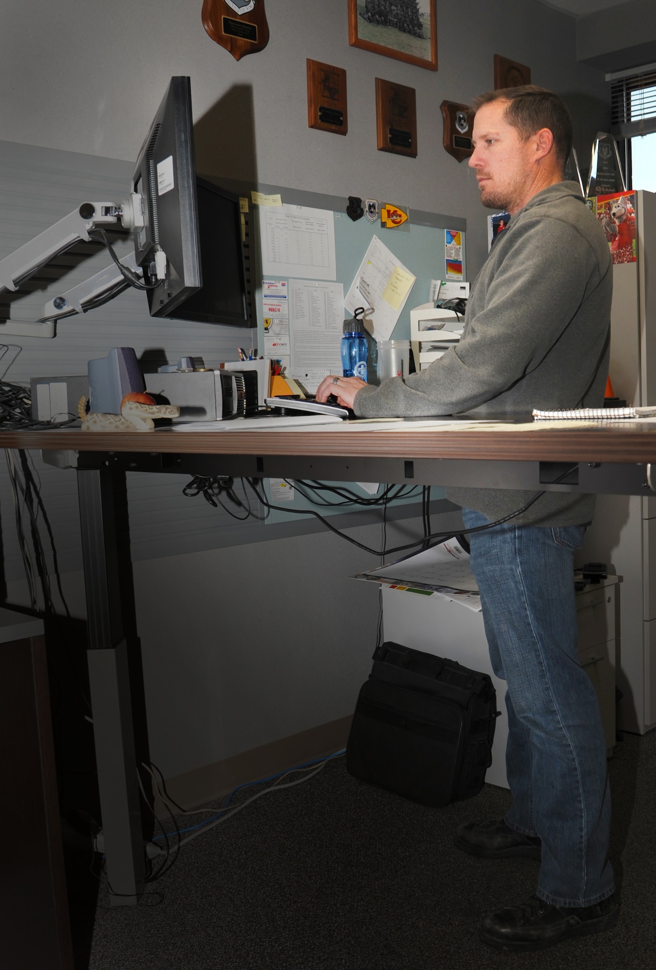Master Sgt. Justin Johnson, a manager in the 442d Fighter Wing Safety Office, spends his workday alternating between standing at his desk and lowering it to sit. Johnson advocates considering a standing work center because of the health benefits of avoiding excessive sedentary hours in a day. (Photo by the 442d Fighter Wing)
