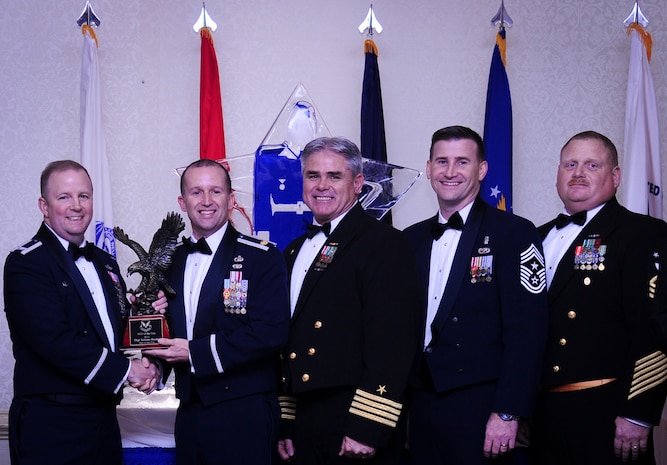 Col. Jeffrey DeVore, Joint Base Charleston commander, Capt. Timothy Sparks, JB Charleston deputy commander, Master Chief Petty Officer Joseph Gardner, Naval Support Activity command master chief and Chief Master Sgt. Mark Bronson, 628th Air Base Wing command chief present Maj. Samuel Shmip, 628th Comptroller Squadron commander, with the NCO of the year award Jan. 23, 2015, at the 2015 628th ABW Annual Awards Banquet at the Charleston Club on Joint Base Charleston, S.C. Shimp is accepting the award for Tech. Sgt. Toriano Banks, who is currently deployed. (U.S. Air Force photo/Airman 1st Class Clayton Cupit)