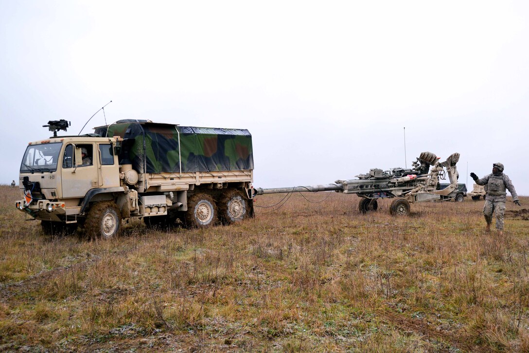 A U.S. soldier gives direction to another soldier driving a truck to move an M777 howitzer into firing position for a live-fire exercise at the 7th Army Joint Multinational Training Command’s Grafenwoehr Training Area, Germany, Jan. 23, 2015. The soldiers are assigned to Battery B, Field Artillery Squadron, 2nd Cavalry Regiment.