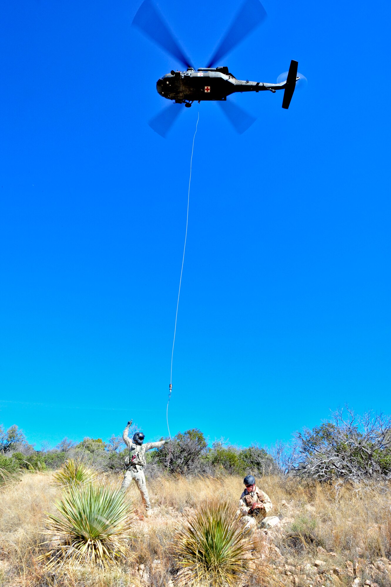 Arizona Army National Guard Sgt. Kevin Murphy, Detachment 1, C Company, 5-159th Air Ambulance flight medic, signals to his crew chief in the UH-60A Black Hawk helicopter above while U.S. Air Force Airman 1st Class Andrew Stranger, 355th Operations Support Squadron intelligence analyst, simulates an injured downed pilot during a joint training exercise held in southern Arizona, Jan. 20, 2015.  The joint training consisted of A-10C Thunderbolt IIs from the 354th Fighter Squadron, based out of Davis-Monthan Air Force Base, and the UH-60A Black Hawk helicopter from Detachment 1, C Company, 5-159th Air Ambulance, based out of Phoenix, conducting close air support and combat search and rescue exercises.  (U.S. Air Force Photo by Airman 1st Class Chris Massey/Released)