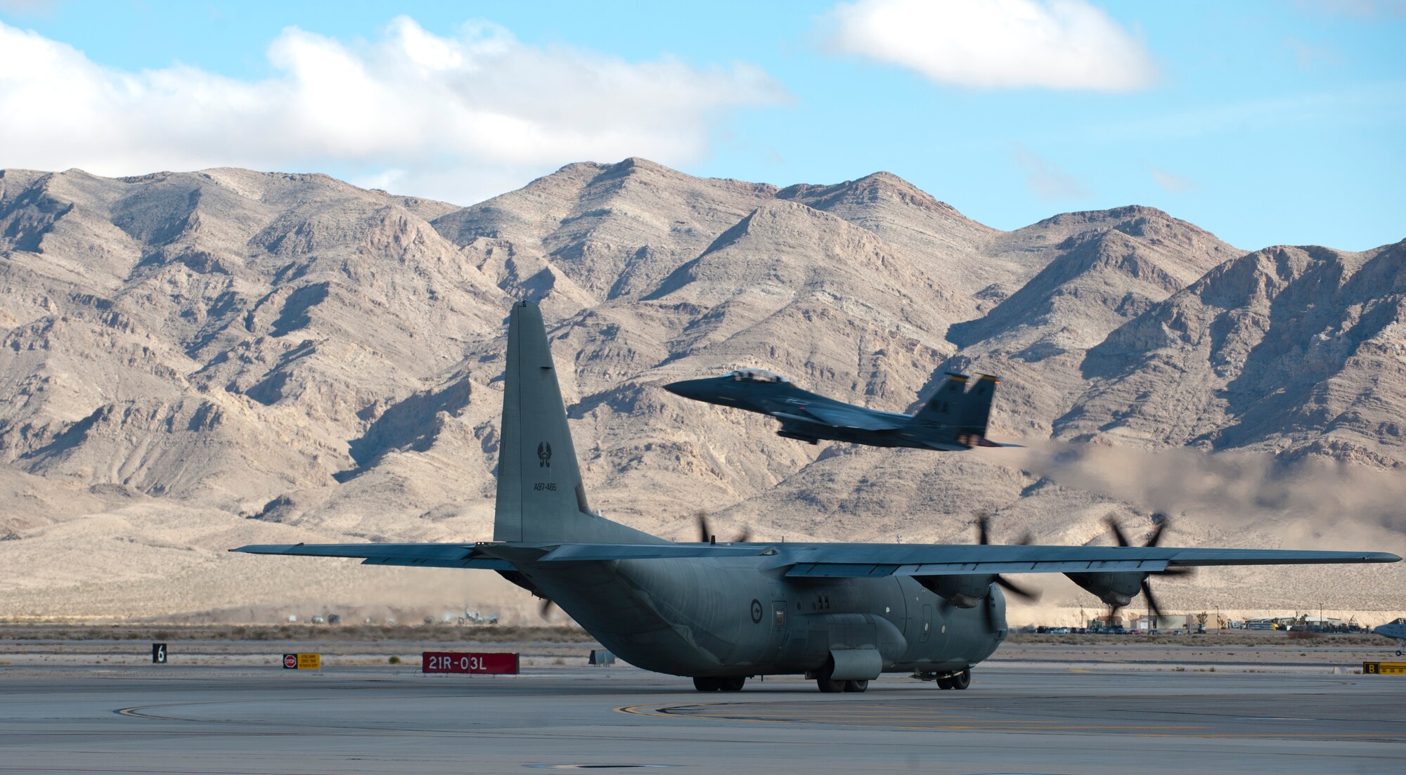 A Royal Australian air force C-130J Super Hercules assigned to 37 Squadron, RAAF Richmond, Australia, taxis to the runway during Red Flag 15-1, as an F-15 Eagle assigned to the U.S. Air Force Weapons School takes off at Nellis Air Force Base, Nev., Jan. 27, 2015. Flying units from around the globe deploy to Nellis AFB to participate in Red Flag. The exercise is held three to four times a year and is organized by the 414th Combat Training Squadron. (U.S. Air Force photo by Senior Airman Thomas Spangler)