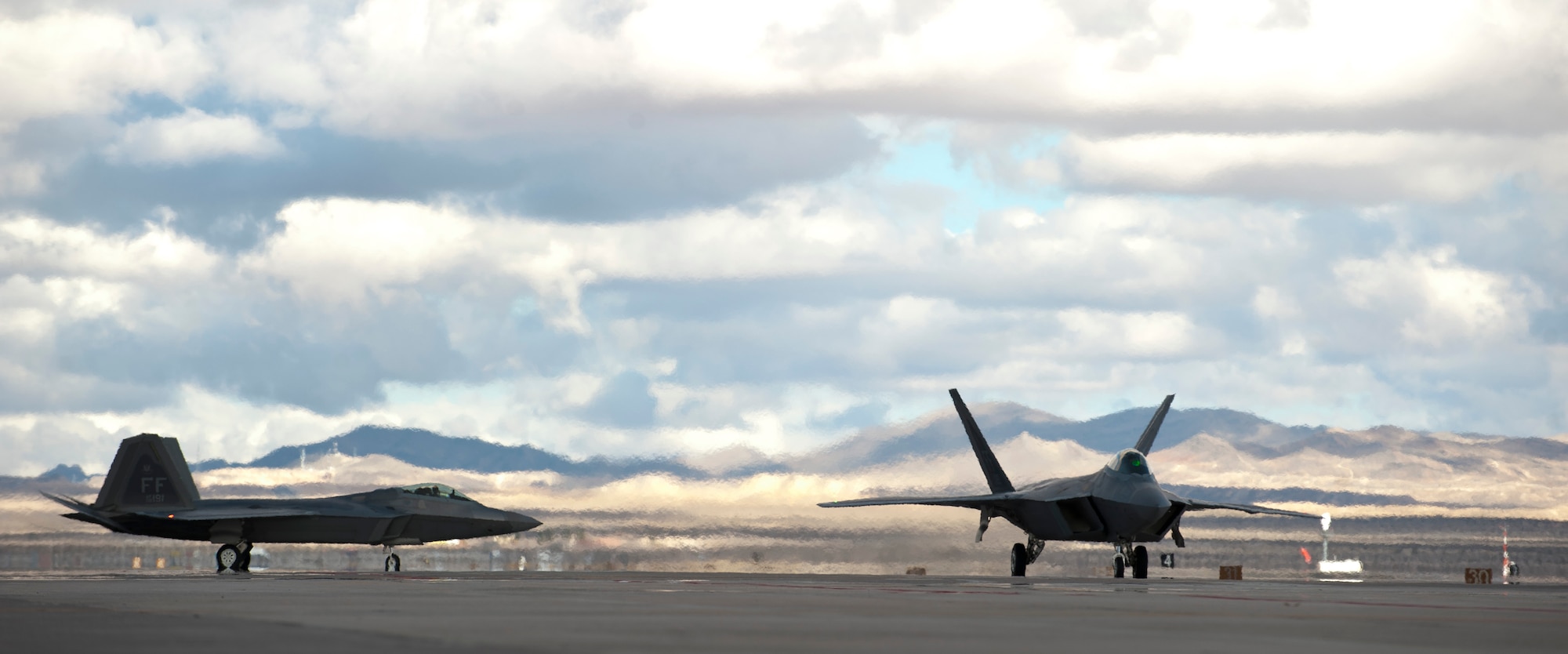 Two F-22 Raptors assigned to the 94th Fighter Squadron from Joint Base Langley-Eustis, Va., taxi to the runway during Red Flag 15-1 at Nellis AFB, Nev., Jan. 27, 2015. Red Flag is one of a series of advanced training programs administered by the U.S. Air Force Warfare Center designed to increase combat readiness and effectiveness. (U.S. Air Force photo by Senior Airman Thomas Spangler)