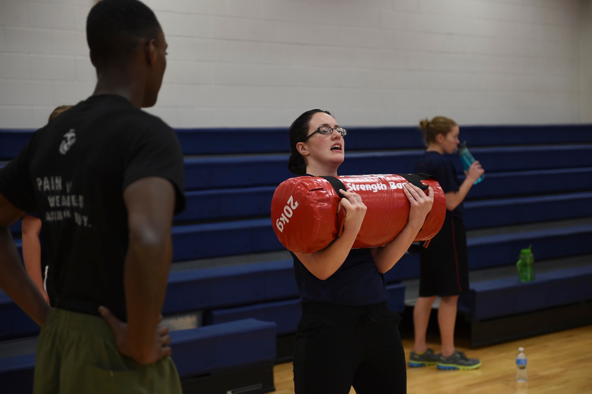 A U.S. Marine Corps poolee squats with a sandbag while a Marine looks on during a delayed entry program all-female workout held Jan. 17, 2015, at the fitness center on Buckley Air Force Base, Colo. Poolees are members of the DEP that have not yet shipped out to recruit training. The DEP workouts consist of strengthening exercises to enable the poolees to be accustomed to the vigorous workouts and stress they will endure once they arrive at recruit training. (U.S. Air Force photo by Airman 1st Class Samantha Saulsbury/Released)