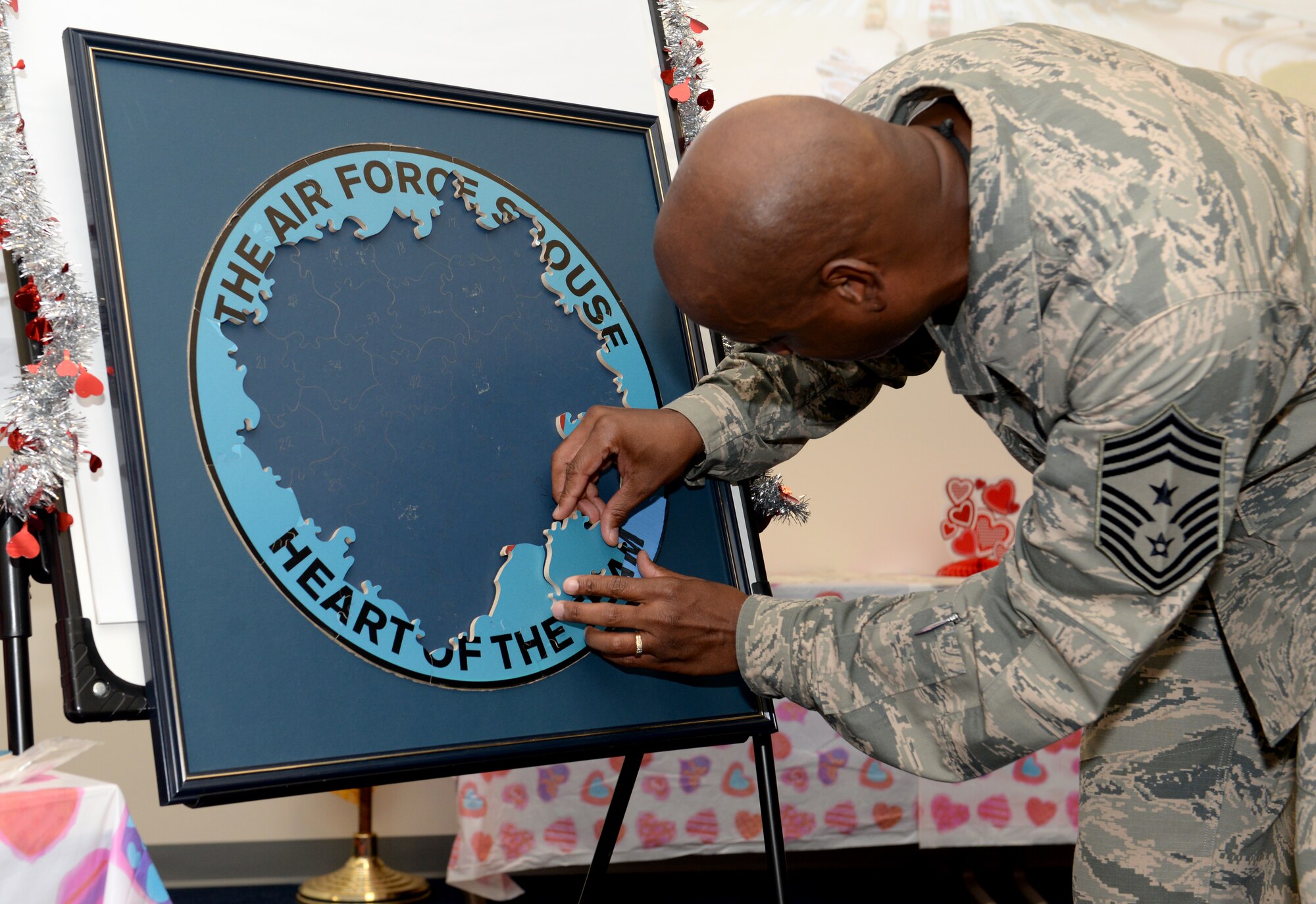 Chief Master Sgt. Michael McMillan, 36th Wing command chief master sergeant, attaches a puzzle piece during the Heart Link Spouses Workshop Jan. 26, 2015, at Andersen Air Force Base, Guam. The puzzle forms the Heart Link logo; wings to represent the Air Force, an airplane to represent the Air Force mission, and a red contrail to represent the “link” of spouses as the heart of the Air Force team. (U.S. Air Force photo by Senior Airman Amanda Morris/Released)