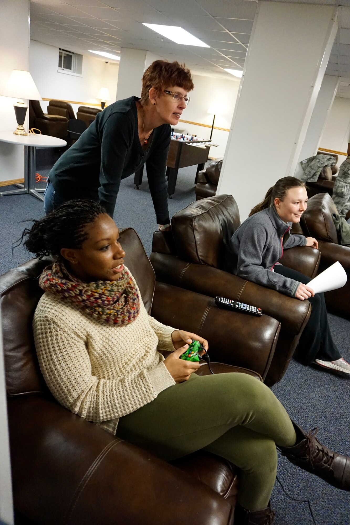 Airman 1st Class DeAnaira Preyear, 90th Missile Security Forces Squadron, plays a video game as Debbie Ellgen, the Oasis program coordinator, and Airman 1st Class Madison Nelson, 90th MSFS, watch  in the Oasis Airman Ministry Center on F.E. Warren Air Force Base, Wyo., Jan. 26, 2015. The Oasis is a chapel-sponsored ministry center where Airmen can relax with such amenities as a pool table, foosball table, darts, video gaming, and cable TV (U.S. Air Force photo/Lan Kim)
