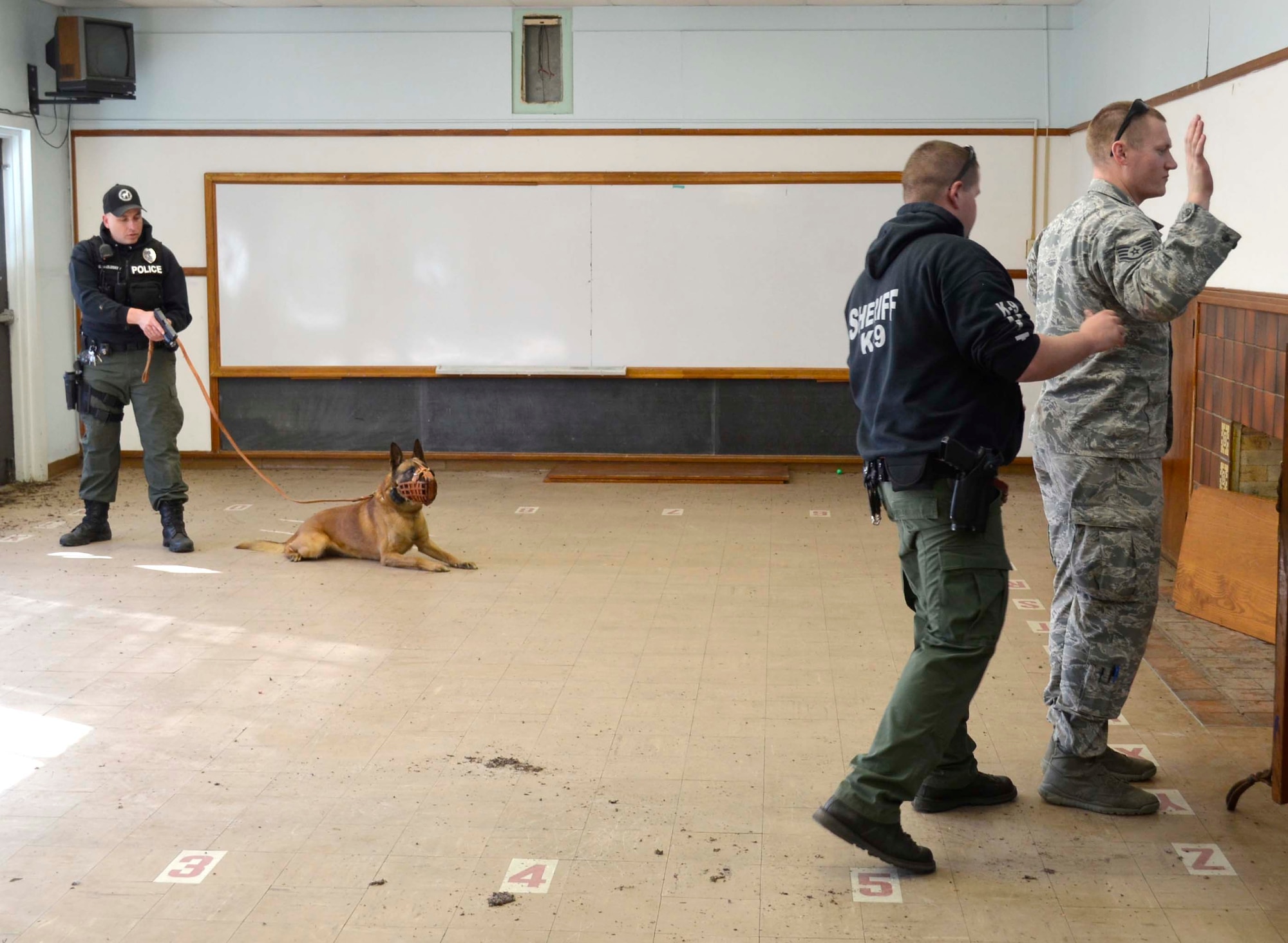 (Left) Sgt. Chad McCluskey, Augusta Department of Public Safety K-9 handler, supervises as (right) Staff Sgt. Kyle Quigg, 22nd Security Forces Squadron military working dog handler, is searched for contraband during a training exercise, Jan. 27, 2015, in Independence, Kan.  McConnell security forces worked with local police departments to practice handling a variety of real-life scenarios. (Courtesy photo)