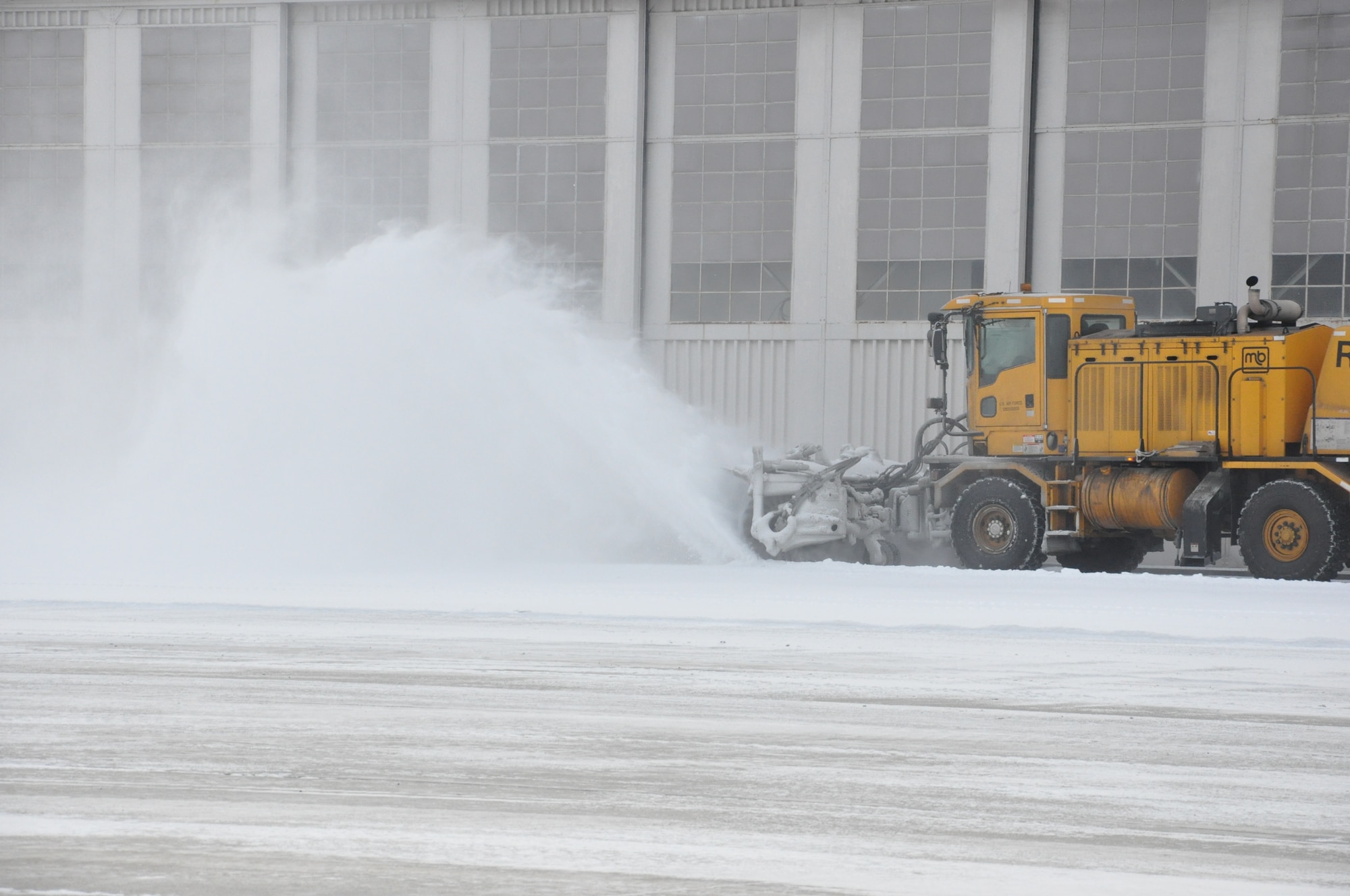 During Jan. 26 snowfall, Bob Orr operates the snow broom, throwing a plume of snow as he clears the airfield for Base Operations. The airfield is top priority and receives attention first. (Air Force photo by Sandy Simison)
