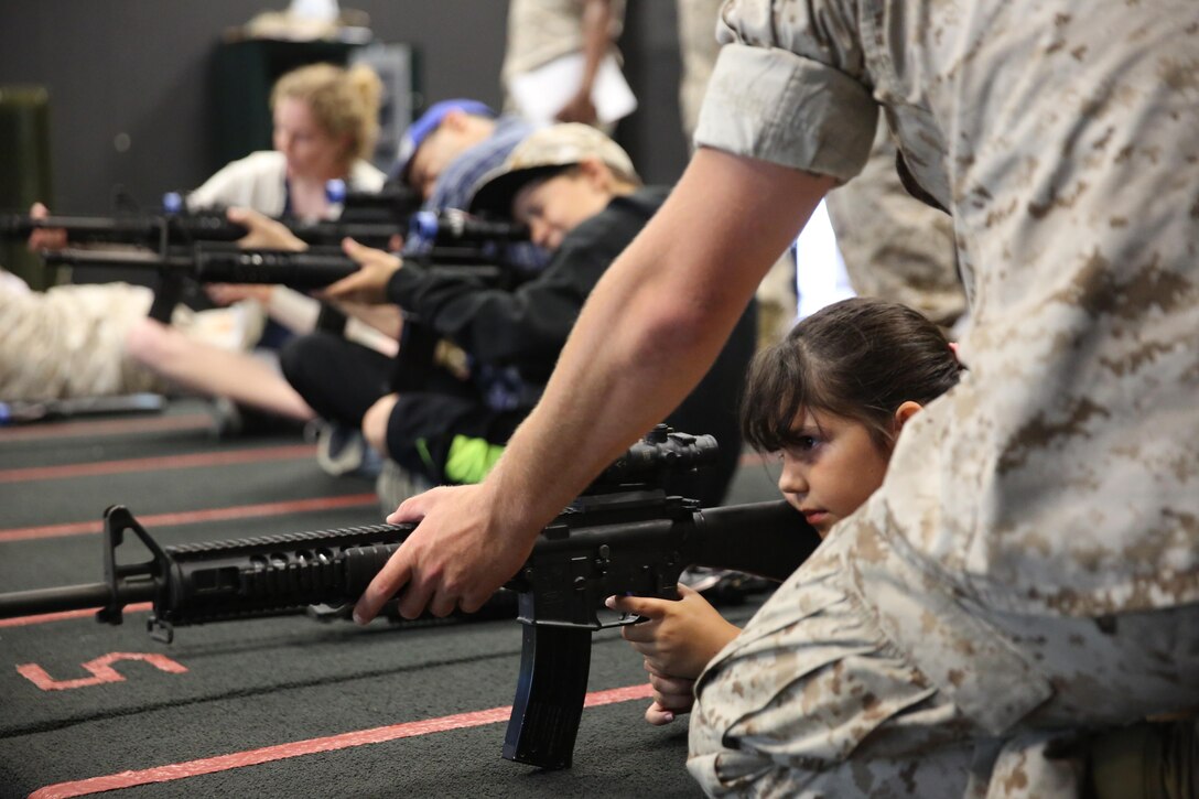 Summer Sosa, daughter of Chief Warrant Officer Alexander Sosa, an expeditionary airfield and emergency services officer with Headquarters and Headquarters Squadron, looks through the scope of a training rifle under the supervision of a marksmanship coach during the Devil Dog Family Day aboard Marine Corps Air Station Miramar, California, June 26. The Devil Dog Family Day allowed Marines to bring their family members to different locations on MCAS Miramar to learn more about the Marine Corps.