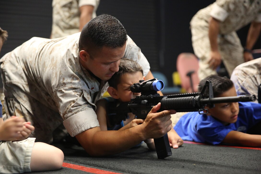 Chief Warrant Officer Alexander Sosa, an expeditionary airfield and emergency services officer with Headquarters and Headquarters Squadron, supervises his son with a training rifle at the Indoor Simulated Marksmanship Trainer aboard Marine Corps Air Station Miramar, California, June 26. Marines, spouses and children visited several locations to learn about Marine Corps jobs, weapons and training during Devil Dog Family Day.