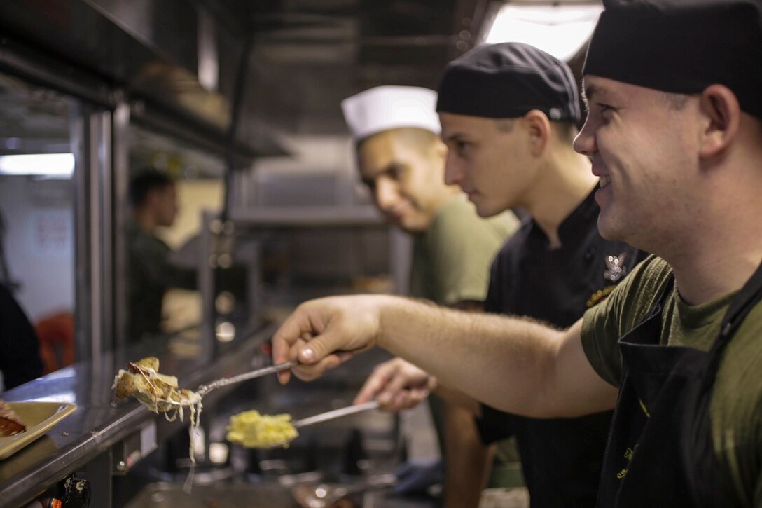U.S. Marine Lance Cpl. Cody Fann, right, and U.S. Navy Petty Officer 2nd Class Eathan Hendrix, left, serve food in the mess deck of the San Antonio-class amphibious transport dock ship USS Anchorage (LPD 23).  Anchorage is part of the Essex Amphibious Ready Group and, with the embarked 15th Marine Expeditionary Unit, is deployed in support of maritime security operations and theater security cooperation efforts in the U.S. 5th Fleet area of operations. (U.S. Marine Corps photo by Sgt. Jamean Berry/Released)