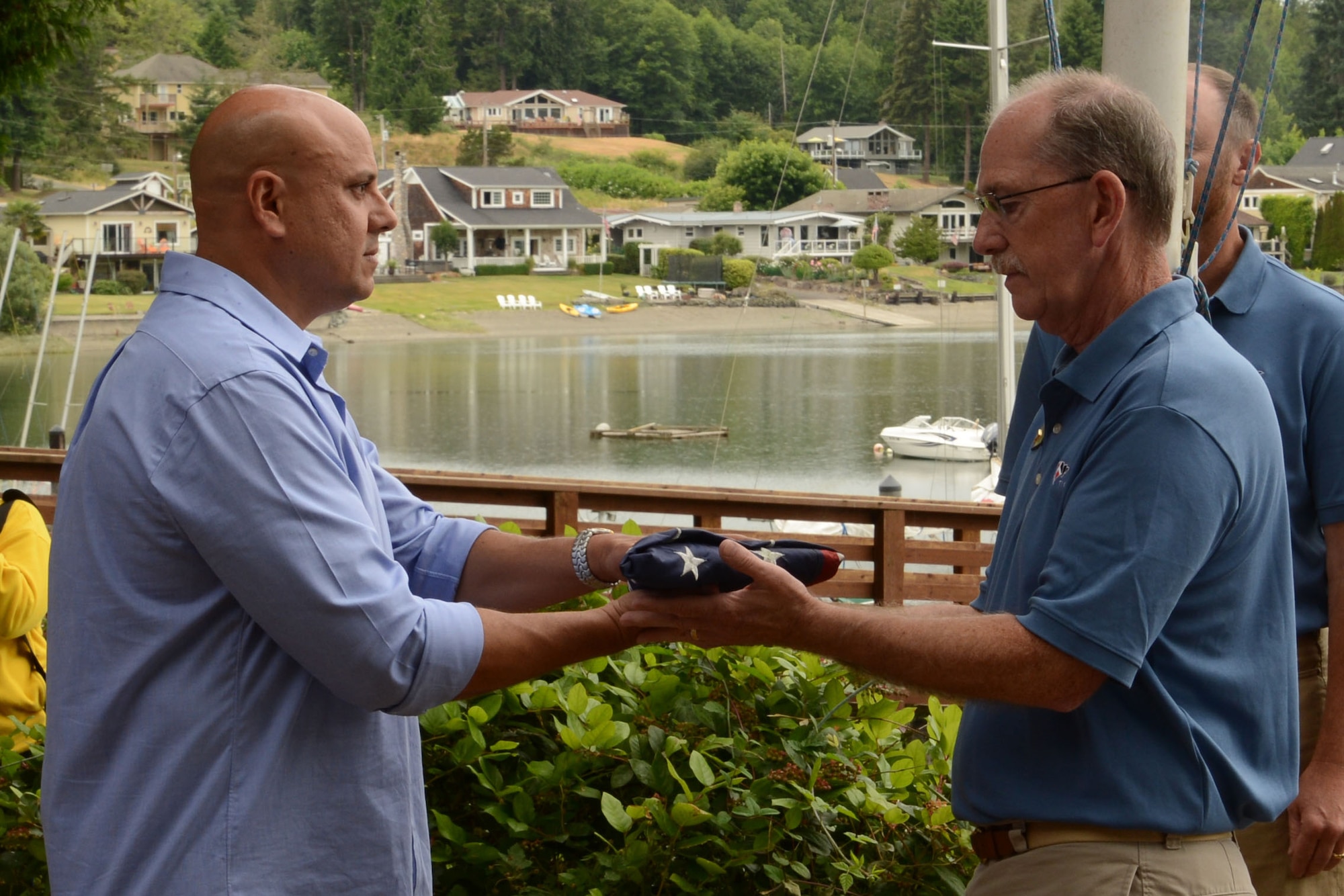 Chief Master Sgt. Zaki Mazid, 62nd Airlift Wing command chief, passes the American flag to a member of the Tacoma Yacht Club, June 24, 2015, at Wollochet Bay Outstation in Gig Harbor, Wash., during the flag raising ceremony at the 2015 Evergreen Fleet Cruise. The Evergreen Fleet Cruise event begins with a breakfast at the Tacoma Yacht Club, followed by a cruise to Wollochet Bay Outstation in the Puget Sound for a picnic lunch, and ends with a cruise back to the Tacoma Yacht Club. (U.S. Air Force photo\Staff Sgt. Katie Jackson)