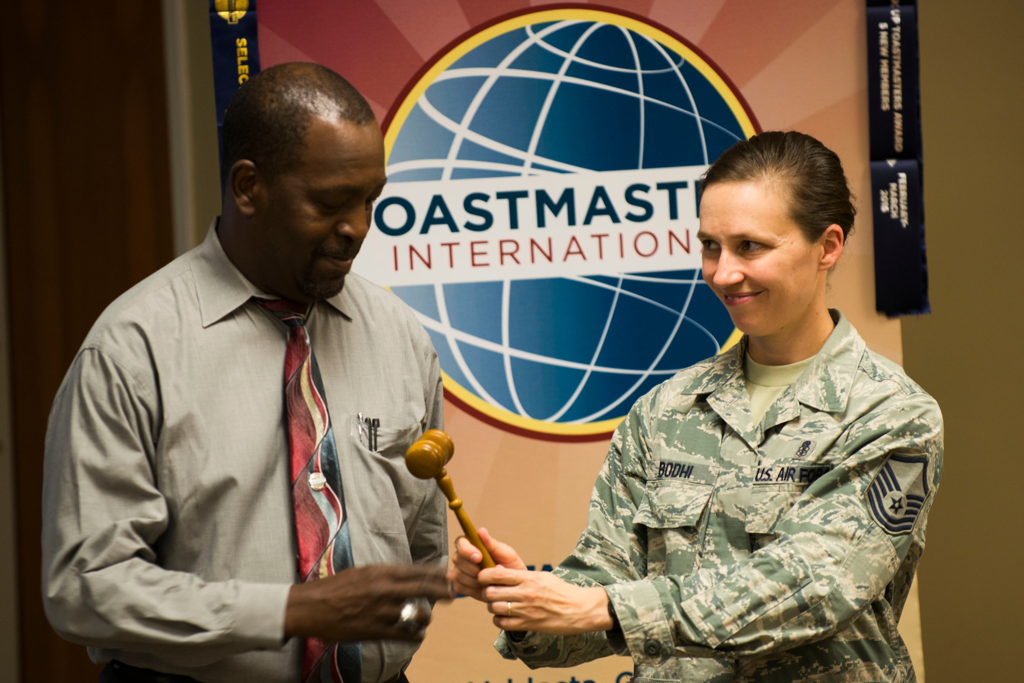 U.S. Air Force Master Sgt. Evita Bodhi,(right) Moody Talking Tigers vice president of membership, passes a Toastmasters gavel to Jerry Bullard, incoming MTT president, during the 2015 MTT inauguration ceremony June 25, 2015, at Moody Air Force Base, Ga. Talking Tigers leadership pass the gavel to show relinquishing their position during the ceremony. (U.S. Air Force photo by Airman 1st Class Dillian Bamman/Released)