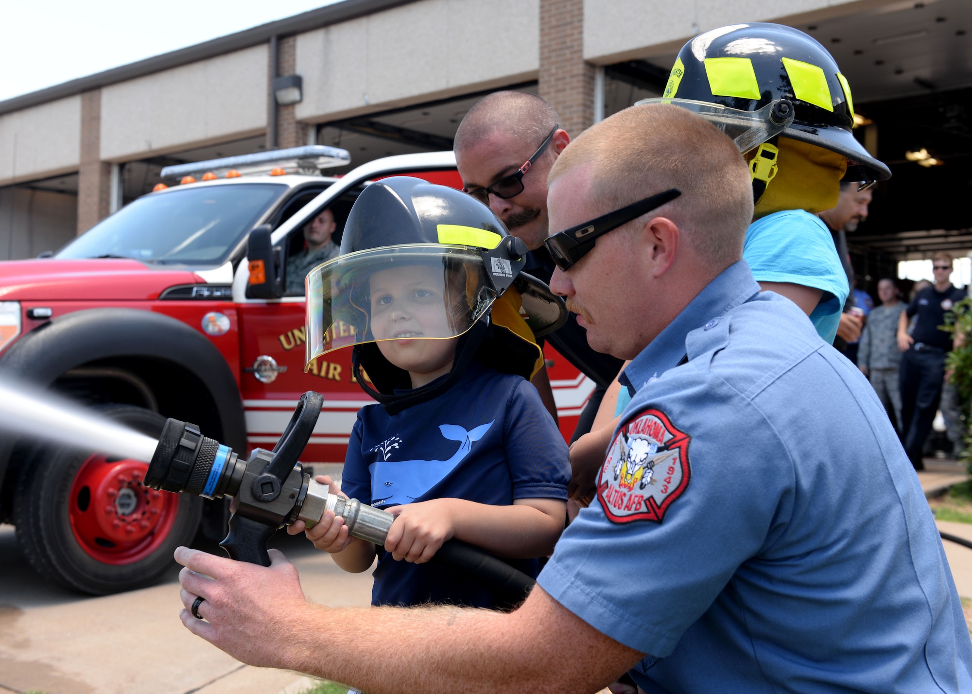 ALTUS AIR FORCE BASE, Okla. – Jaxon Dugger sprays a fire hose with members of the 97th Civil Engineer Squadron fire department at the fire house, June 26, 2015. Members of the 97th CES fire department also drove Jaxon from the front gate to the 58th Airlift Squadron that morning for his Pilot for a Day mission briefing. (U.S. Air Force photo by Airman 1st Class Kirby Turbak/Released)