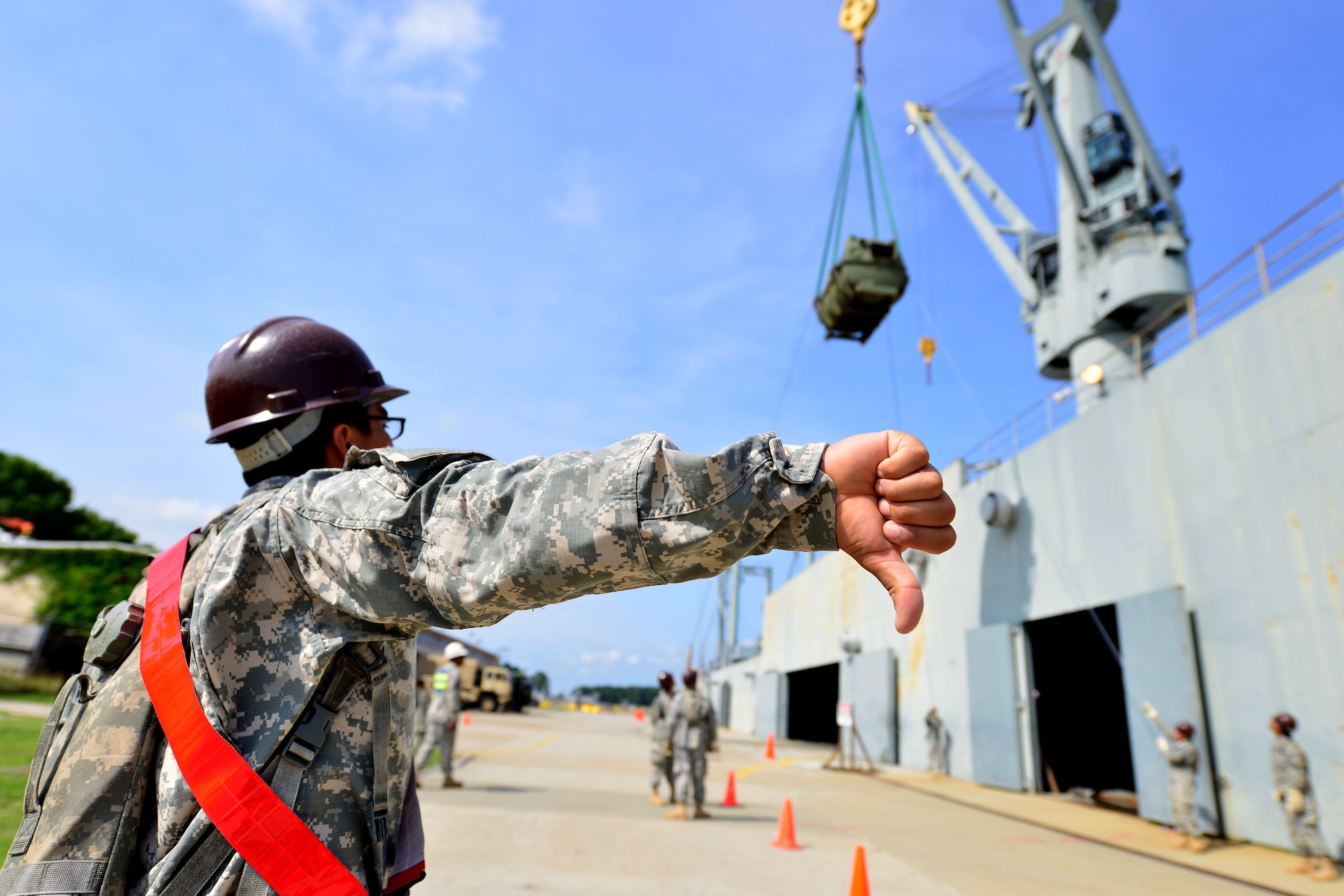 U.S. Army Spc. Francisco Estrada, Transportation School cargo specialist course student, signals to the crane operator during a cargo training exercise at Fort Eustis, Va., June 25, 2015. Throughout, the exercise, Soldiers switched positions to get hands-on training with the various aspects of port terminal transportation operations. (U.S. Air Force photo by Staff Sgt. Natasha Stannard/Released)