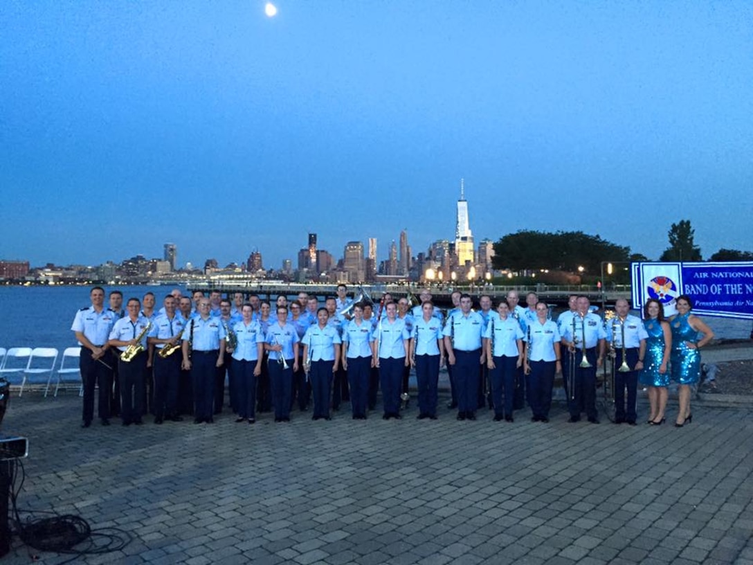 The Air National Guard Band of the Northeast takes the opportunity to take a group photo in Sinatra Park, Hoboken NJ on Monday June 29. The New York City skyline and the Freedom Tower are lit up for night in the background.