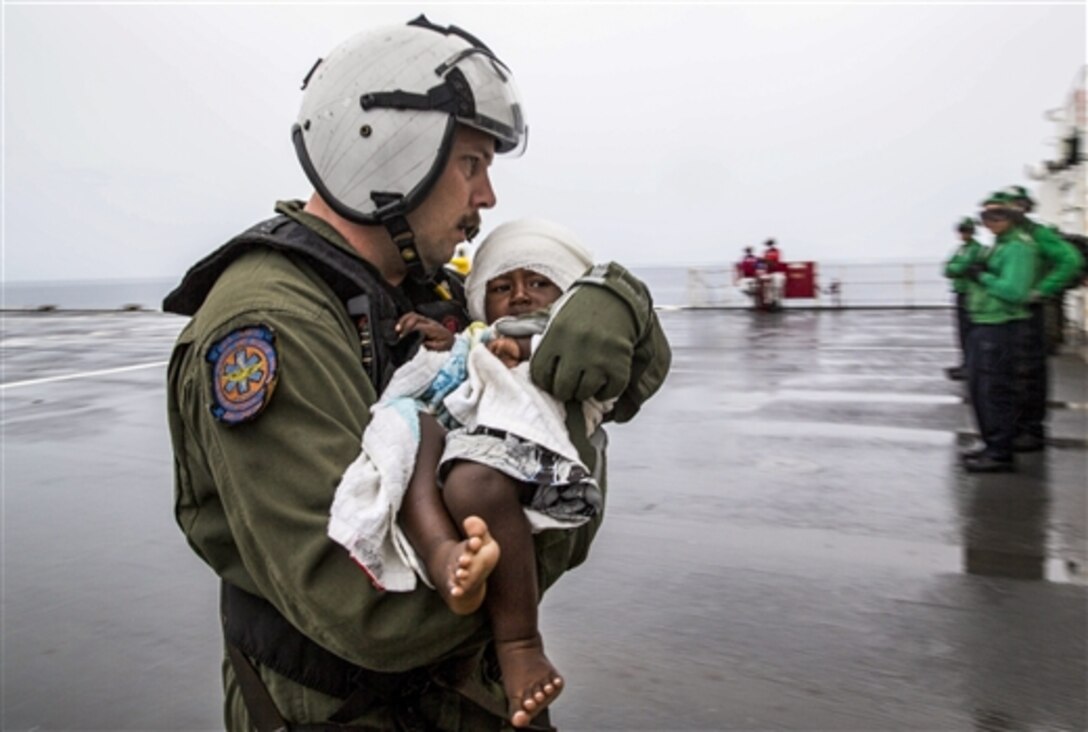 U.S. Navy Petty Officer 1st Class Matthew Hawkins carries an infant aboard the Military Sealift Command hospital ship USNS Mercy in the waters off Papua New Guinea, June 30, 2015. At the request of the government, the Mercy launched a helicopter to transport six passengers, including one infant, who swam ashore after their ship sank. Hawkins is a hospital corpsman assigned to Helicopter Sea Combat Squadron.