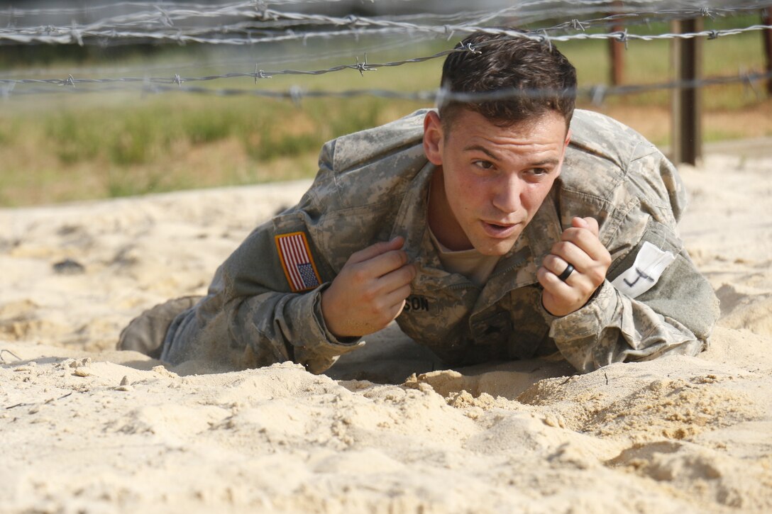 Army Sgt. Joe Anderson crawls through a sand pit underneath barbed wire ...