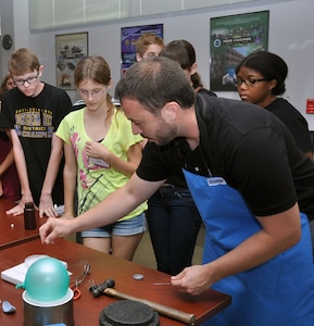 NSWCDD hosted the Fredericksburg Regional Governor's School on June 25.  Students from the counties of Caroline, King George, Spotsylvania, Stafford, Fredericksburg City, and other private schools in the region were given tours of NSWCDD's unique facilities - Ground Plane area, Chemical Biological Radiological (CBR) Defense Laboratory, Railgun Facility, and Human Systems Integration Laboratory.  Dr. Bryan Tienes, Chemist, CBR Concepts & Experimentation Branch (NSWCDD Z21) used the cryogenic capabilities of liquid nitrogen in a demonstration focused on highlighting the relationship between a material's temperature and its physical properties.  In the photo, Dr. Tienes is exhibiting the phenomenon of a magnet levitating over a low temperature superconductor chilled with liquid nitrogen.  