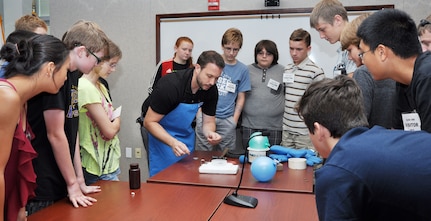 NSWCDD hosted the Fredericksburg Regional Governor's School on June 25.  Students from the counties of Caroline, King George, Spotsylvania, Stafford, Fredericksburg City, and other private schools in the region were given tours of NSWCDD's unique facilities - Ground Plane area, Chemical Biological Radiological (CBR) Defense Laboratory, Railgun Facility, and Human Systems Integration Laboratory.  Dr. Bryan Tienes, Chemist, CBR Concepts & Experimentation Branch (NSWCDD Z21) used the cryogenic capabilities of liquid nitrogen in a demonstration focused on highlighting the relationship between a material's temperature and its physical properties.  In the photo, Dr. Tienes is exhibiting the phenomenon of a magnet levitating over a low temperature superconductor chilled with liquid nitrogen.  