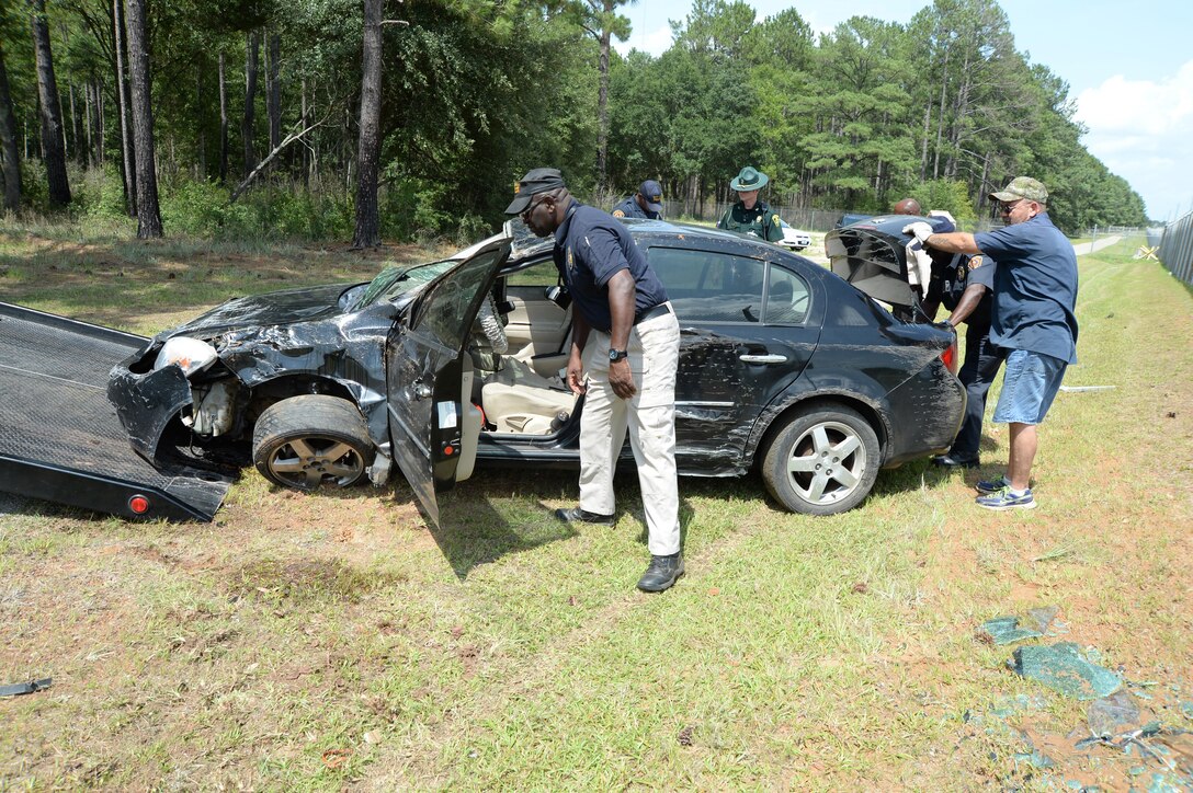 Base officials and local community authorities assess a vehicle involved in a one-car accident along Fleming Road that damaged Marine Corps Logistics Base Albany's fence line, July 1.