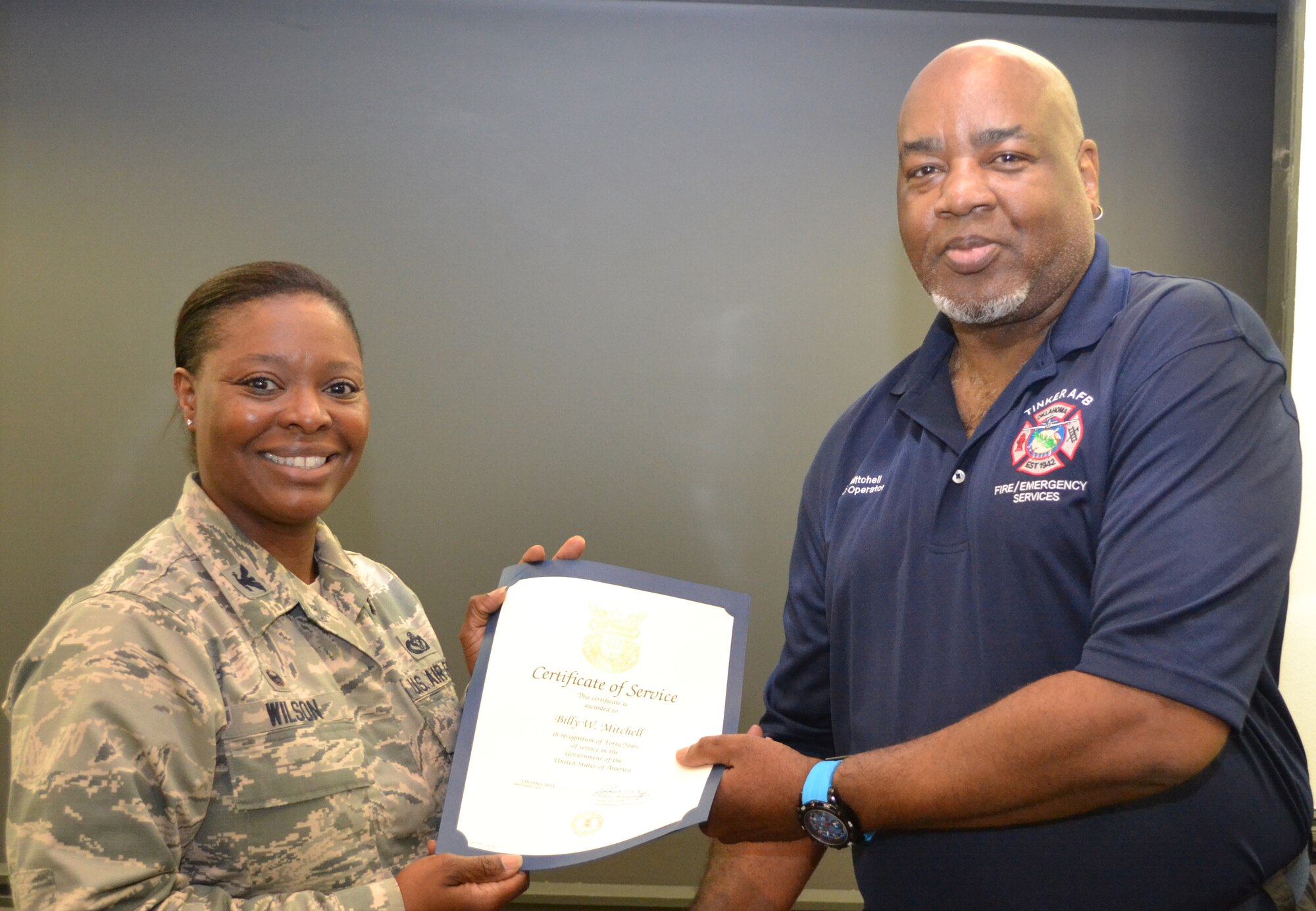 Col. Stephanie Wilson, 72nd Air Base Wing and Tinker installation commander, presents Billy Mitchell, Emergency Communications Center dispatcher at the base fire department, with a certificate and pin recognizing his 40 years of service to the Air Force. (Air Force photo by Ron Mullan/Released)