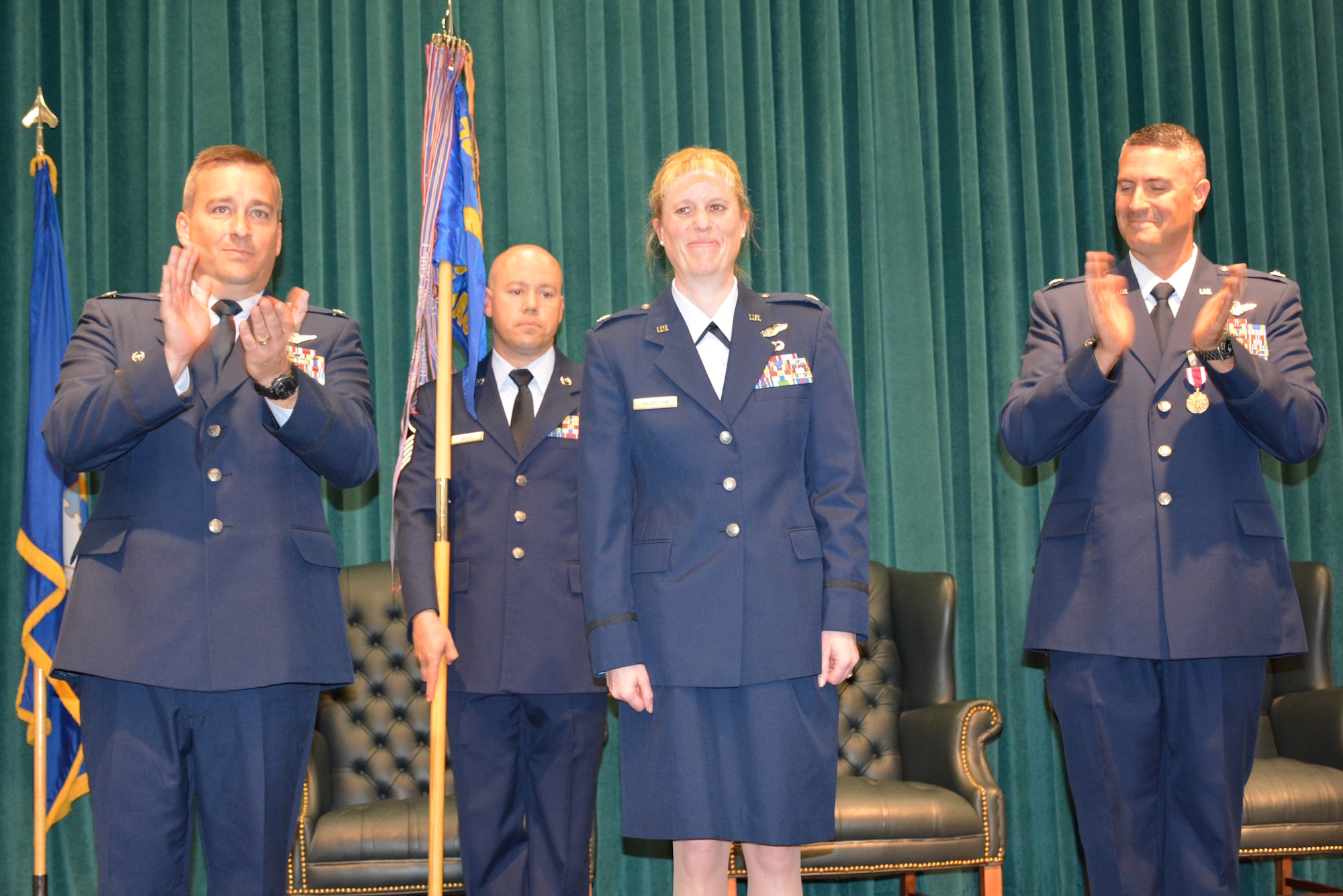 Col. Alain Poisson, 552nd Operations Group commander, left, and Lt. Col. Keven Coyle, outgoing commander of the 960th Airborne Air Control Squadron, lead the congratulatory applause for Lt. Col. Kristen D. Thompson shortly after she assumed command of the squadron during a ceremony Tuesday in Fannin Hall. Holding the guidon is 1st Sgt. Anthony Sayers, 960th AACS. Colonel Poisson presided over the ceremony attended by approximately 100 family members, friends and co-workers. (Air Force photo by Darren D. Heusel/Released)