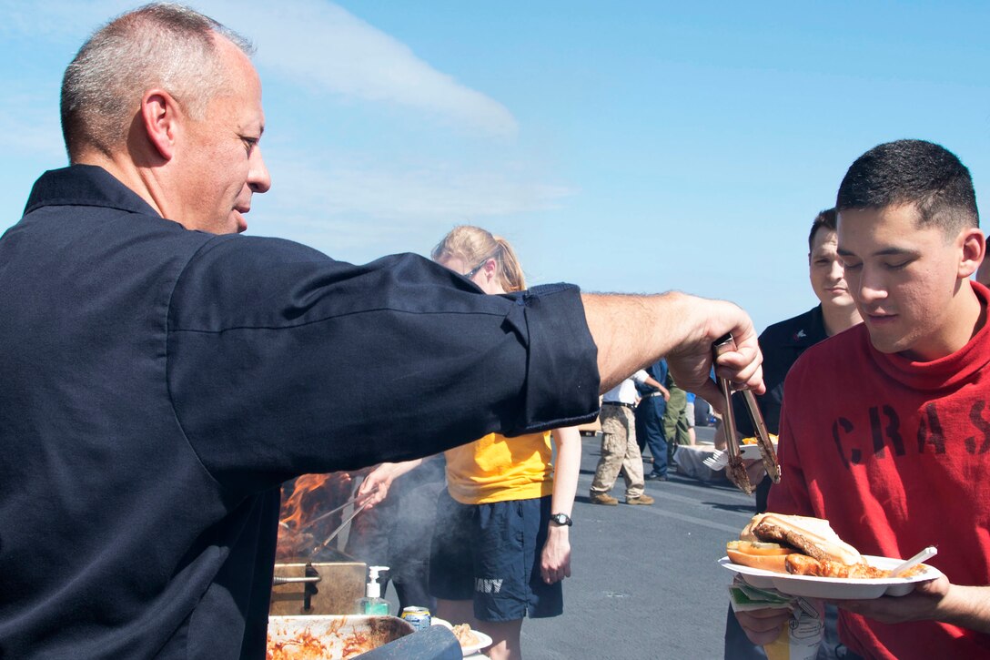 U.S. Navy Capt. Jeffrey Ward, left, commanding officer of the amphibious assault ship USS Bonhomme Richard, cooks and serves hamburgers to the crew during a Fourth of July picnic on the flight deck in the Indian Ocean, July 4, 2015. The Bonhomme Richard is the lead ship of the an expeditionary strike group and is on patrol in the U.S. 7th Fleet area of operations.