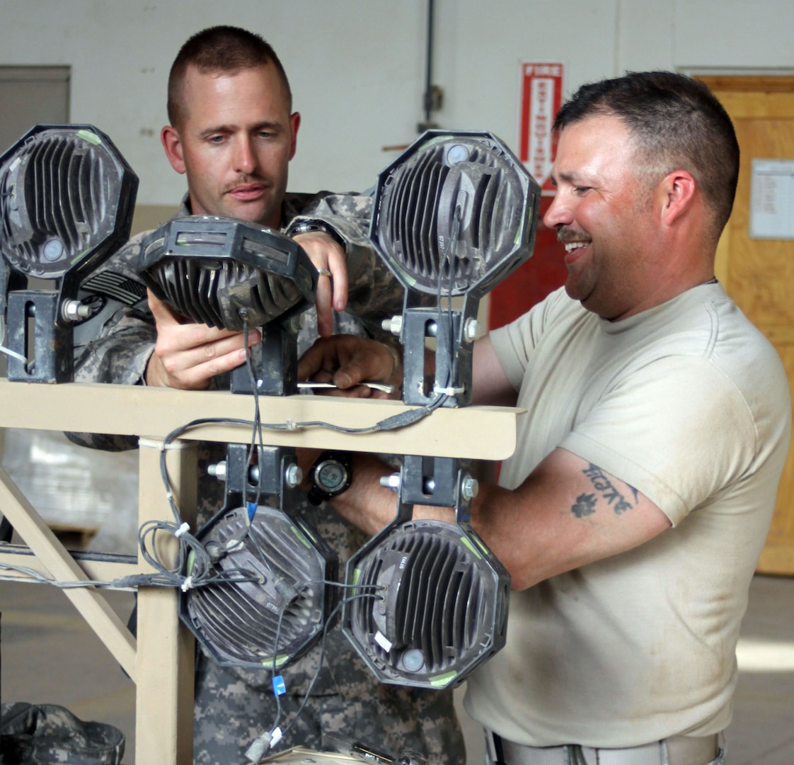 Army Sgt. 1st Class Kevin Dean helps Army Sgt. Mike Main work on a lighting system for a mine resistant ambush protected vehicle at Joint Base Balad, Iraq, April 26, 2011. The Idaho National Guard members are members of the 3rd Battalion, 116th Cavalry Regiment, 77th Sustainment Brigade, 310th Expeditionary Sustainment Personal Security Detachment.