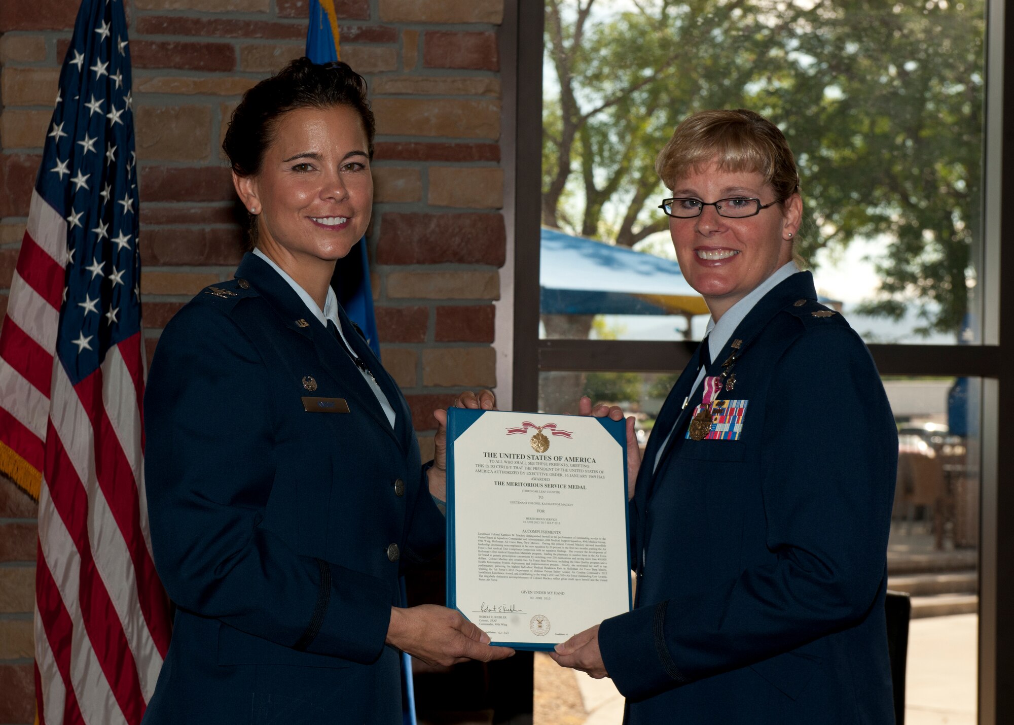 Col. Leslie A. Knight, the 49th Medical Group commander, presents Lt. Col. Kathleen Mackey, the outgoing 49th Medical Support Squadron commander, with an Air Force Meritorious Service Medal on Holloman Air Force Base, N.M., July 7, 2015. Knight was the presiding officer over the formal change of command ceremony where Mackey relinquished command to Lt. Col. Elbert Alford. The 49th MDSS has 77 active duty and civilian personnel who maintain the operation of all medical support activities, medical readiness items, facility management, and pharmacy operations. (U.S. Air Force photo by Senior Airman Chase Cannon/Released)