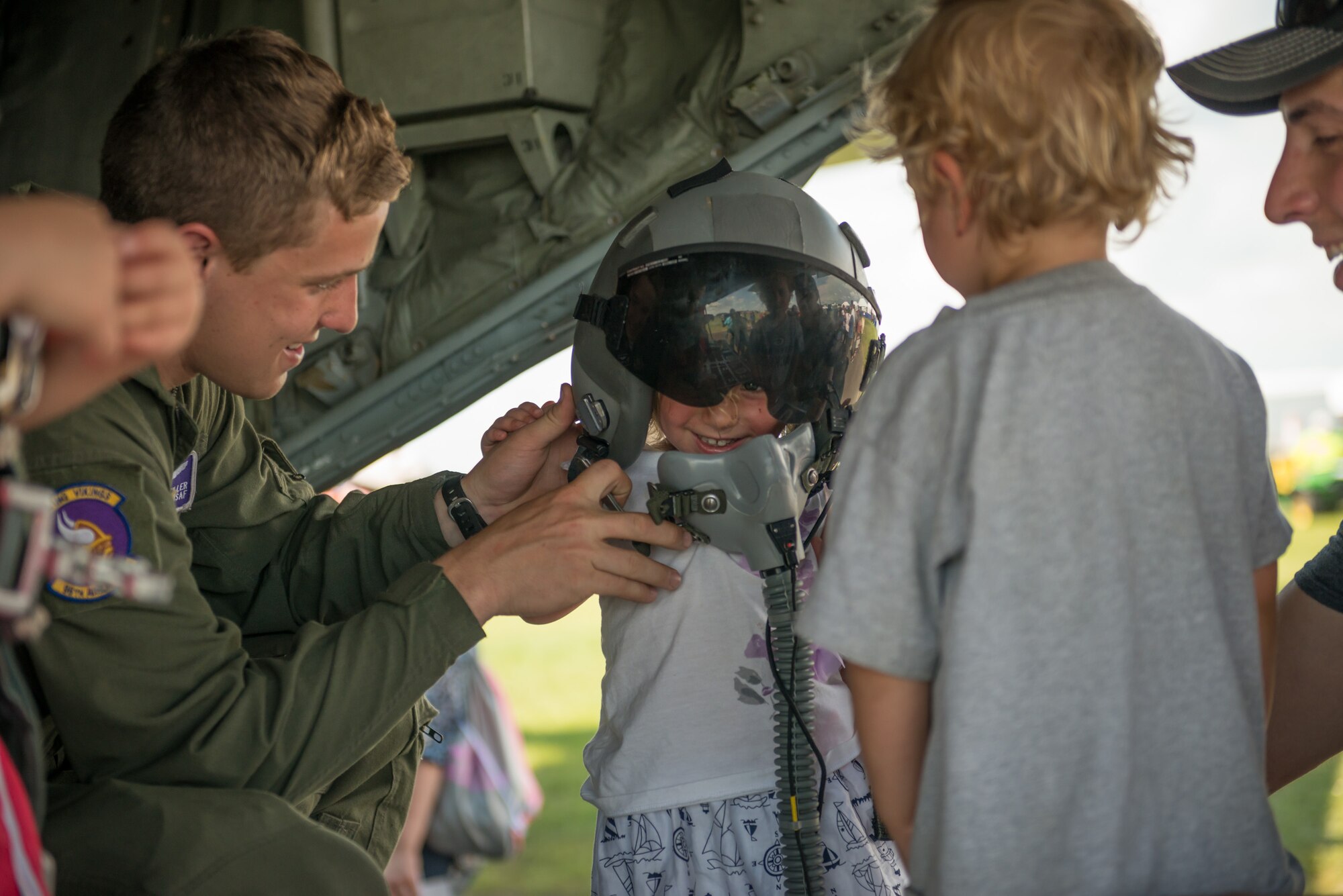 Airman 1st Class Alec Miller, 96th Airlift Squadron, helps a young girl try on a helmet during the Minnesota Air Spectacular in Mankato, Minn.   Members of the 934th Airlift Wing provided static tours of a C-130 aircraft during the air show June 27-28, which also included aerial performances, highlighted by the U.S. Air Force Thunderbirds.  (U.S. Air Force photo by Shannon McKay/Released)
