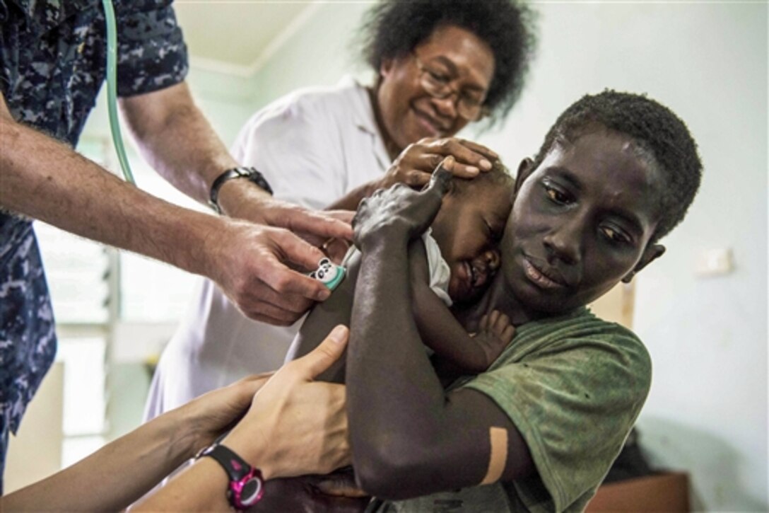A mother holds her daughter while a U.S. sailor and an Arawan nurse examine the baby during a community health engagement at the Arawa Medical Clinic as part of Pacific Partnership 2015 in Arawa in Papua New Guinea, June 29, 2015. 