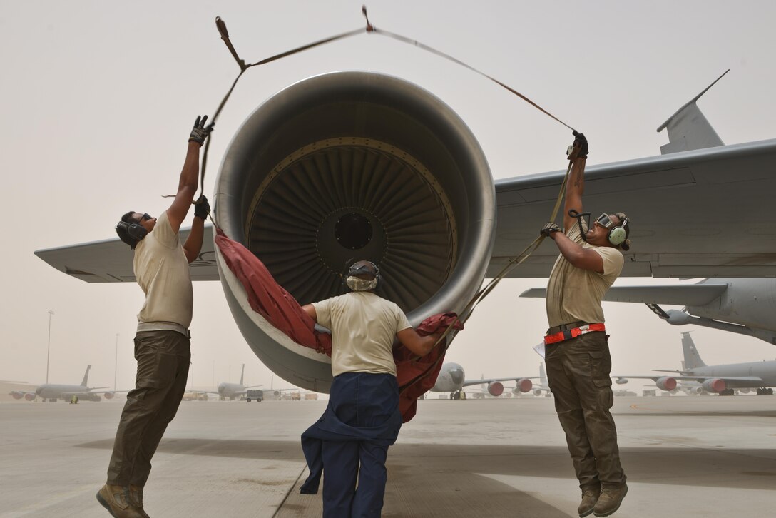 Airman 1st Class Jonathan Palacios-Conde, Senior Airman John Brown and Staff Sgt Marius Kelsey, 340th Expeditionary Aircraft Maintenance Unit, prepare to cover the engine of a KC-135 Stratotanker during a wind storm over 50 knots June 7, 2015 Al Udeid Air Base, Qatar.   