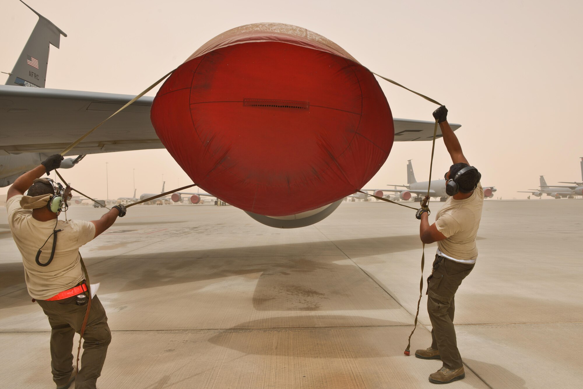 Airman 1st Class Jonathan Palacios-Conde and Senior Airman John Brown, 340th Expeditionary Aircraft Maintenance Unit, prepare to cover the engine of a KC-135 Stratotanker during a wind storm over 50 knots June 7, 2015 Al Udeid Air Base, Qatar.   
