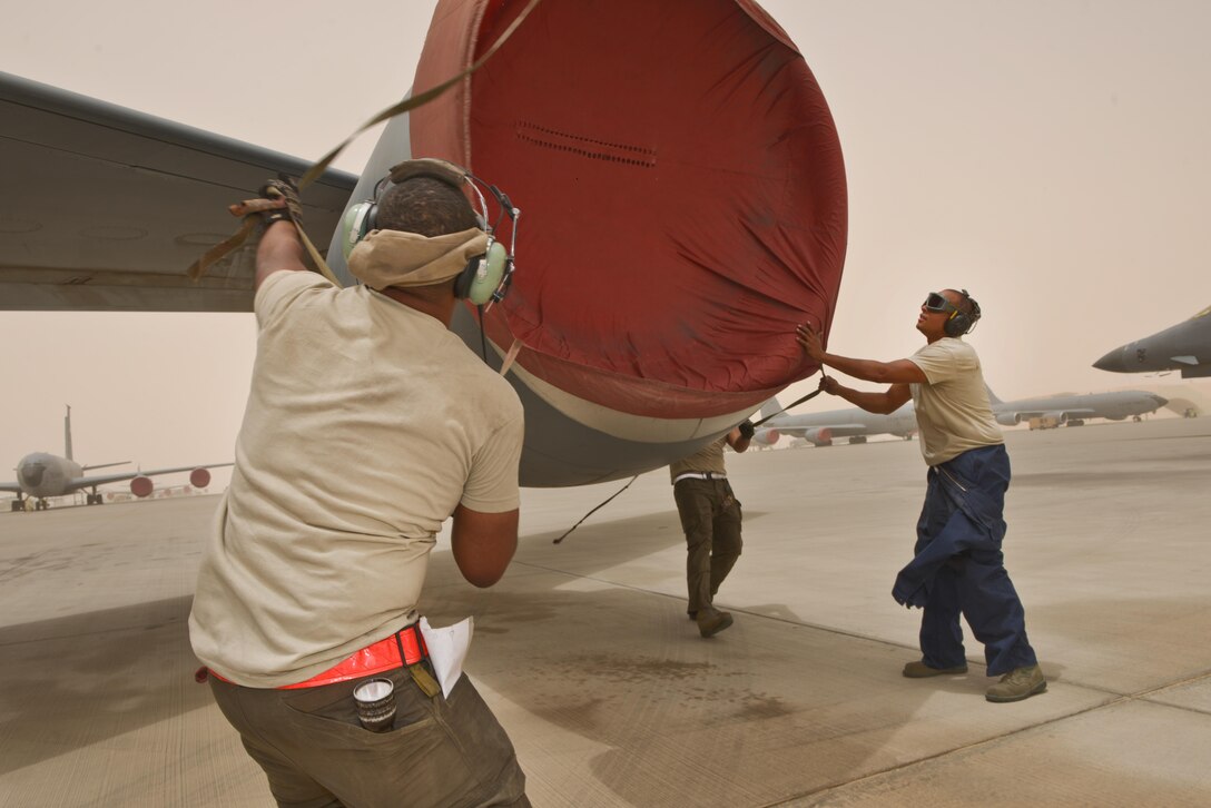 Airman 1st Class Jonathan Palacios-Conde, Senior Airman John Brown and Staff Sgt Marius Kelsey, 340th Expeditionary Aircraft Maintenance Unit, prepare to cover the engine of a KC-135 Stratotanker during a wind storm over 50 knots June 7, 2015 Al Udeid Air Base, Qatar.   
