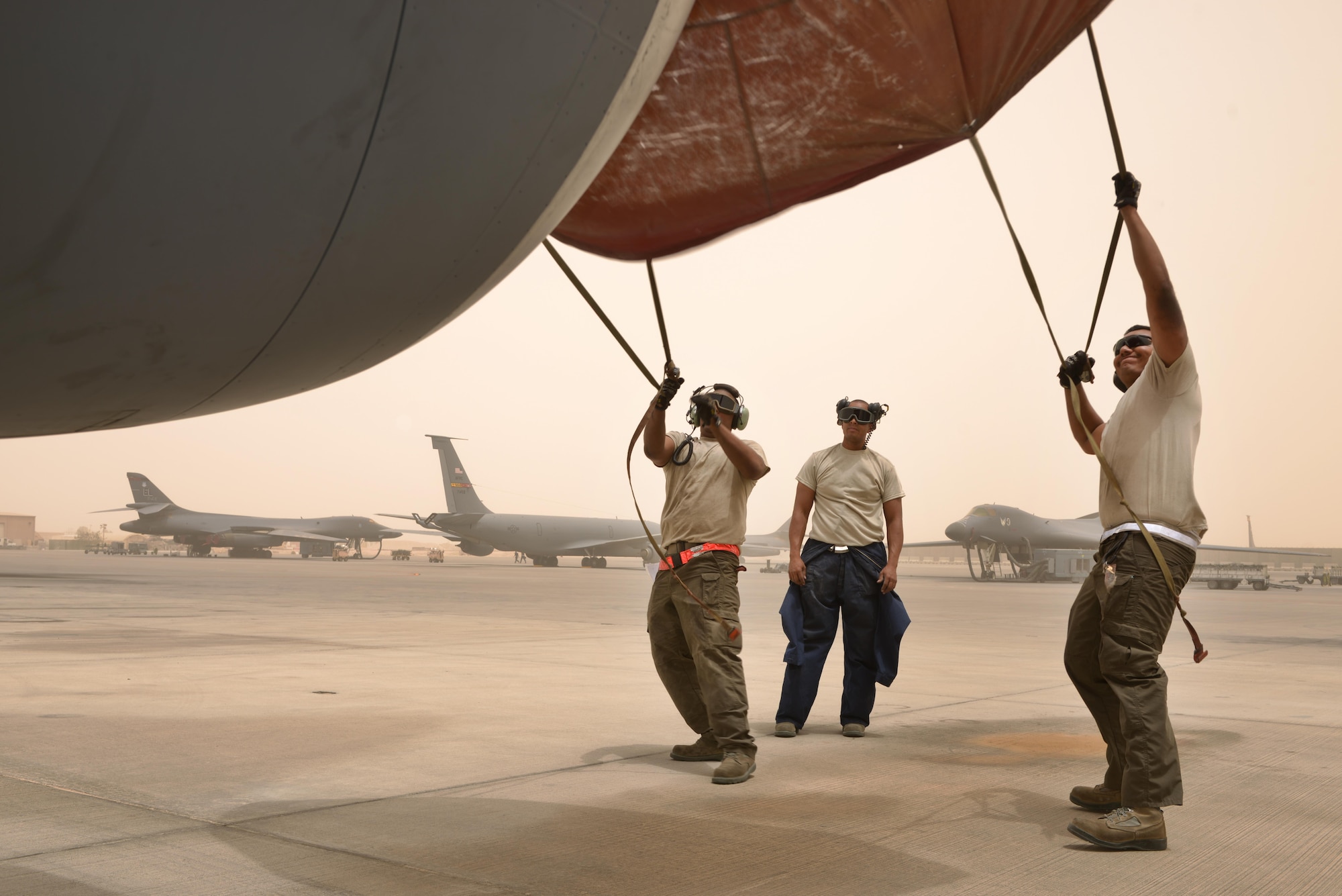 Airman 1st Class Jonathan Palacios-Conde, Senior Airman John Brown and Staff Sgt Marius Kelsey, 340th Expeditionary Aircraft Maintenance Unit, prepare to cover the engine of a KC-135 Stratotanker during a wind storm over 50 knots June 7, 2015 Al Udeid Air Base, Qatar.   