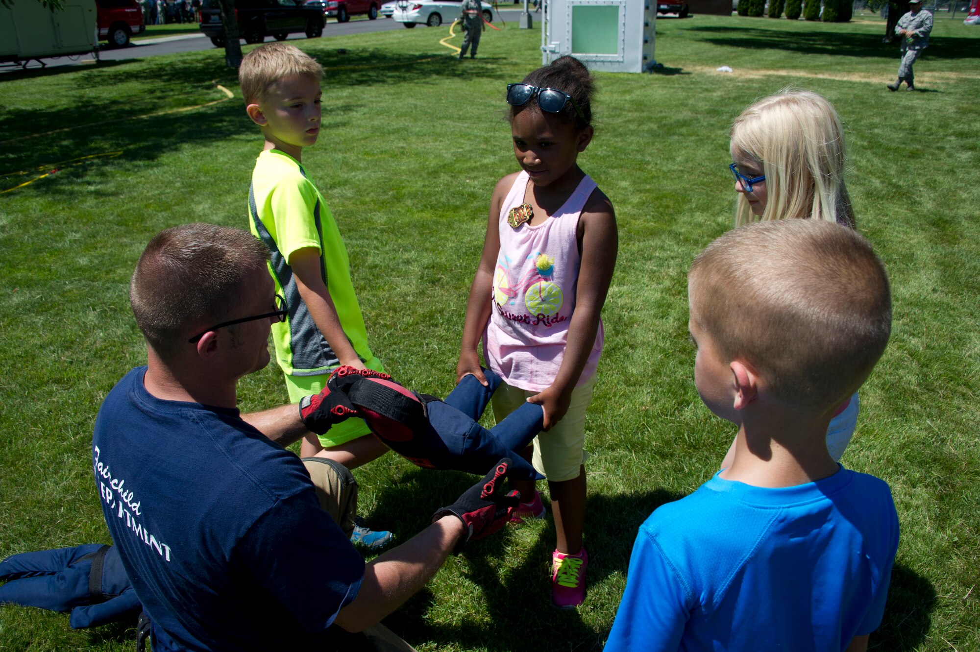 Tech. Sgt. Jacob Wallace, 92nd Civil Engineer Squadron firefighter, shows children from Fairchild's Youth Summer Program  how to properly carry the small mannequin during the buddy carrying event during a summer youth fire prevention camp, July 1, 2015, at Fairchild Air Force Base, Wash. The children learned the importance of working as a team to accomplish the buddy carrying event. (U.S. Air Force photo/Airman 1st Class Nicolo J. Daniello)