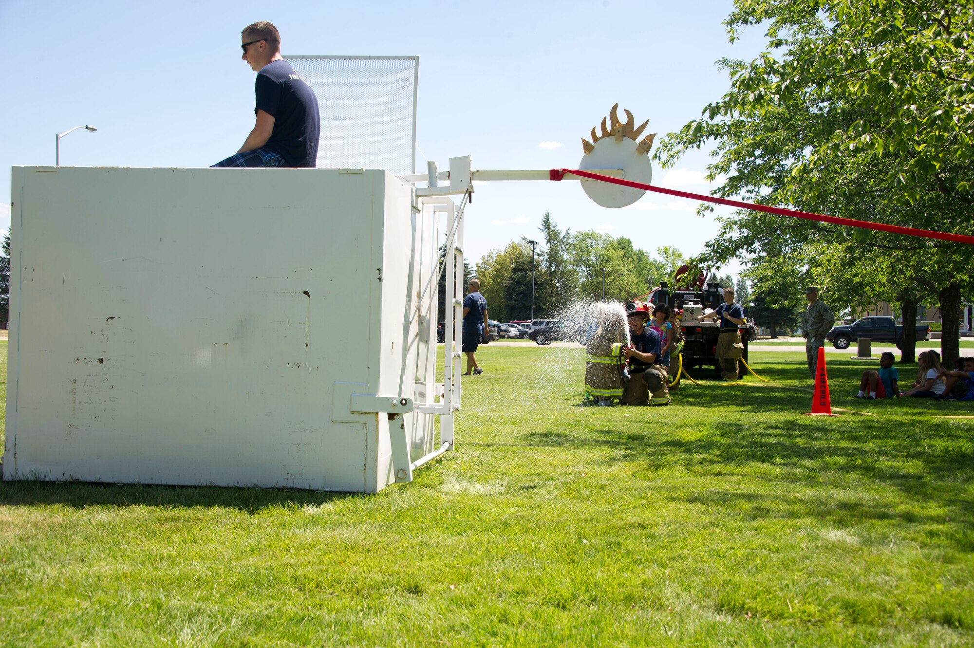 Tech. Sgt. Jacob Wallace, 92nd Civil Engineer Squadron firefighter, assists children from Fairchild's Youth Summer Program by aiming a stream of water at a target during a summer youth fire prevention camp, July 1, 2015, at Fairchild Air Force Base, Wash. The children used a fire hose to spray a target attached to a dunker tank that dropped Senior Airman Aaron Menhart, 92nd CES firefighter, into the water. (U.S. Air Force photo/Airman 1st Class Nicolo J. Daniello)
