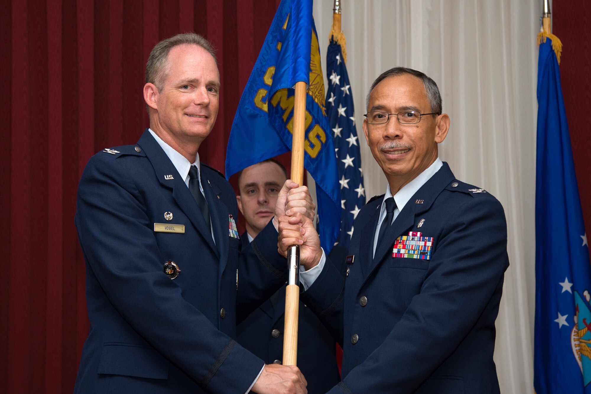 Col. Michael A. Vogel, 66th Air Base Group commander, passes the 66th Medical Squadron guidon to Col. Joel O. Almosara, 66 MDS commander, during a change of command ceremony at the Minuteman Commons July 7, as Master Sgt. Jason Oliver, the squadron's first sergeant, looks on. As commander, Almosara is responsible for all aeromedical services provided to the installation, and more than 200 associated geographically separated units in a seven-state region. (U.S. Air Force photo by Mark Herlihy)