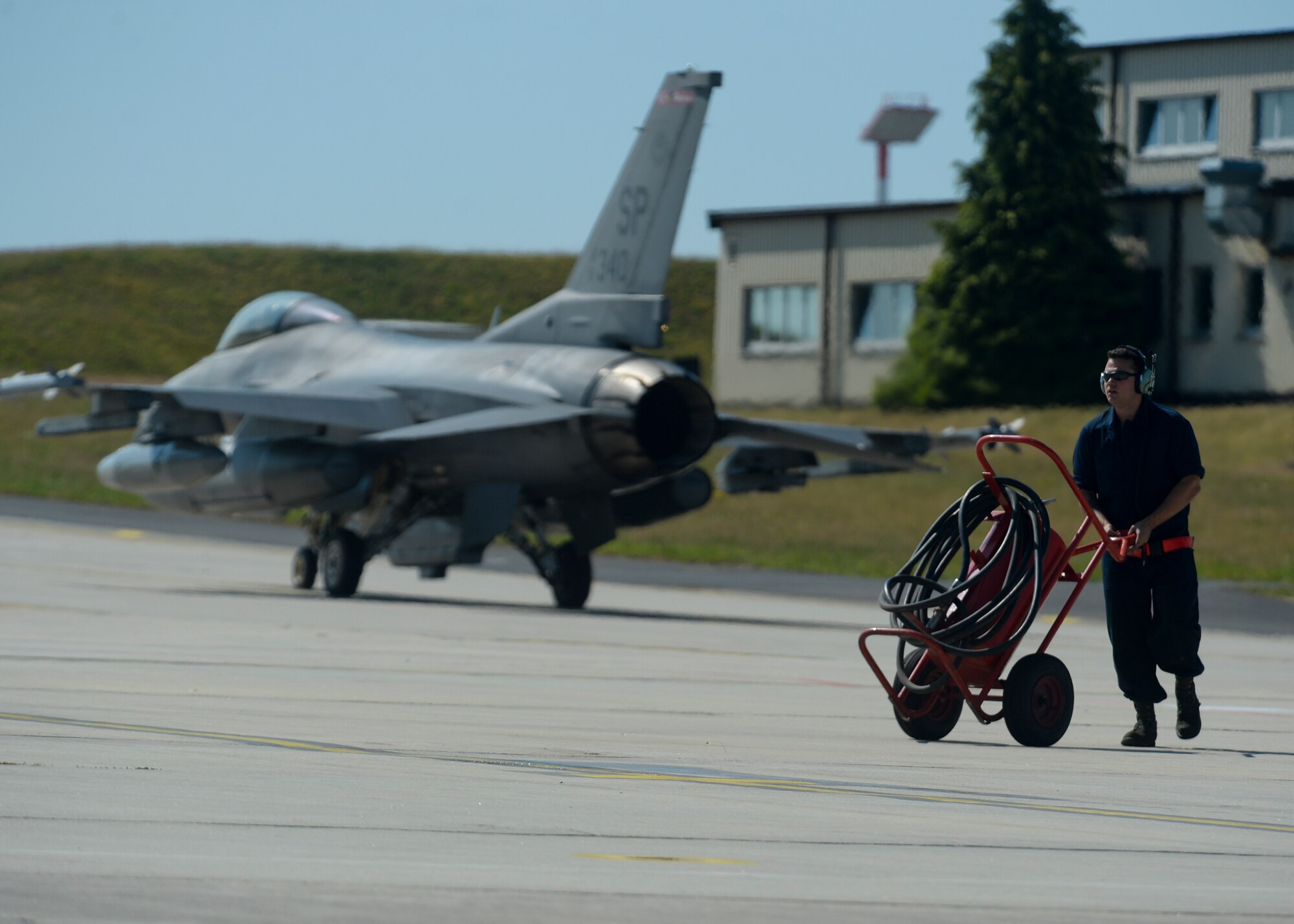 A U.S. Air Force crew chief assigned to the 52nd Aircraft Maintenance Squadron moves maintenance equipment as an F-16 Fighting Falcon fighter aircraft pilot assigned to the 480th Fighter Squadron taxies from the flightline at Spangdahlem Air Base, Germany, July 6, 2015. The aircraft will participate in Red Flag, an exercise which gives pilots an experience of multiple, intensive air combat sorties in the safety of a training environment. (U.S. Air Force photo by Staff Sgt. Joe W. McFadden/Released)