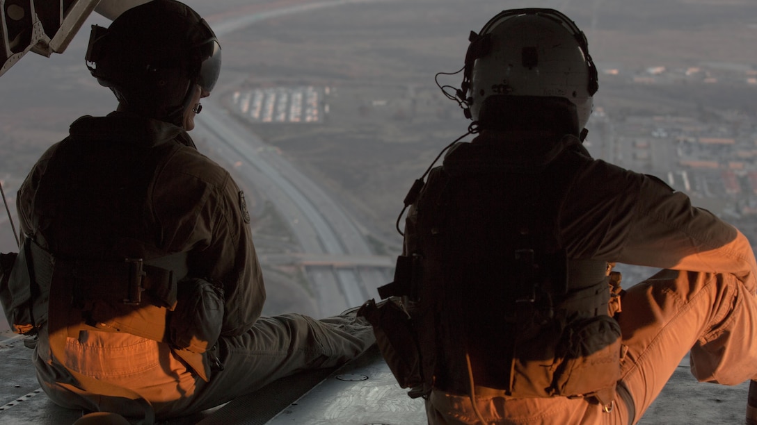 Two crew chiefs with Marine Heavy Helicopter Squadron (HMH) 466 look out the back door of a CH-53E Super Stallion en route to Marine Corps Base Camp Pendleton, California, July 2. The air crew conducted night fast-rope training with Marines from Golf Company, Battalion Landing Team 2nd Battalion, 1st Marine Regiment.