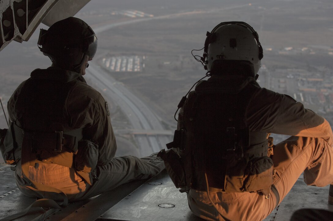 Two crew chiefs with Marine Heavy Helicopter Squadron (HMH) 466 look out the back door of a CH-53E Super Stallion en route to Marine Corps Base Camp Pendleton, California, July 2. The air crew conducted night fast-rope training with Marines from Golf Company, Battalion Landing Team 2nd Battalion, 1st Marine Regiment. (U.S. Marine Corps photo by Sgt. Lillian Stephens/Released)