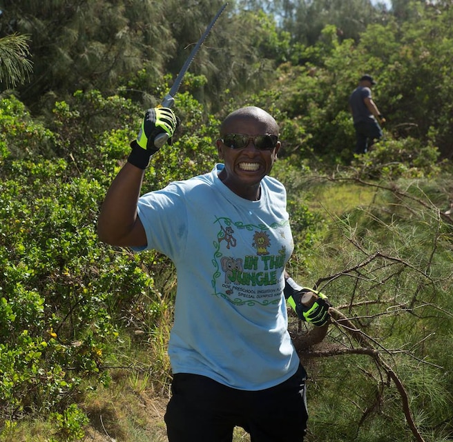 Gunnery Sgt. Jimi Khamisi, a section leader with Marine Wing Support Squadron 374, brandishes his saw after taking down a large branch from an invasive species of plant June 13.