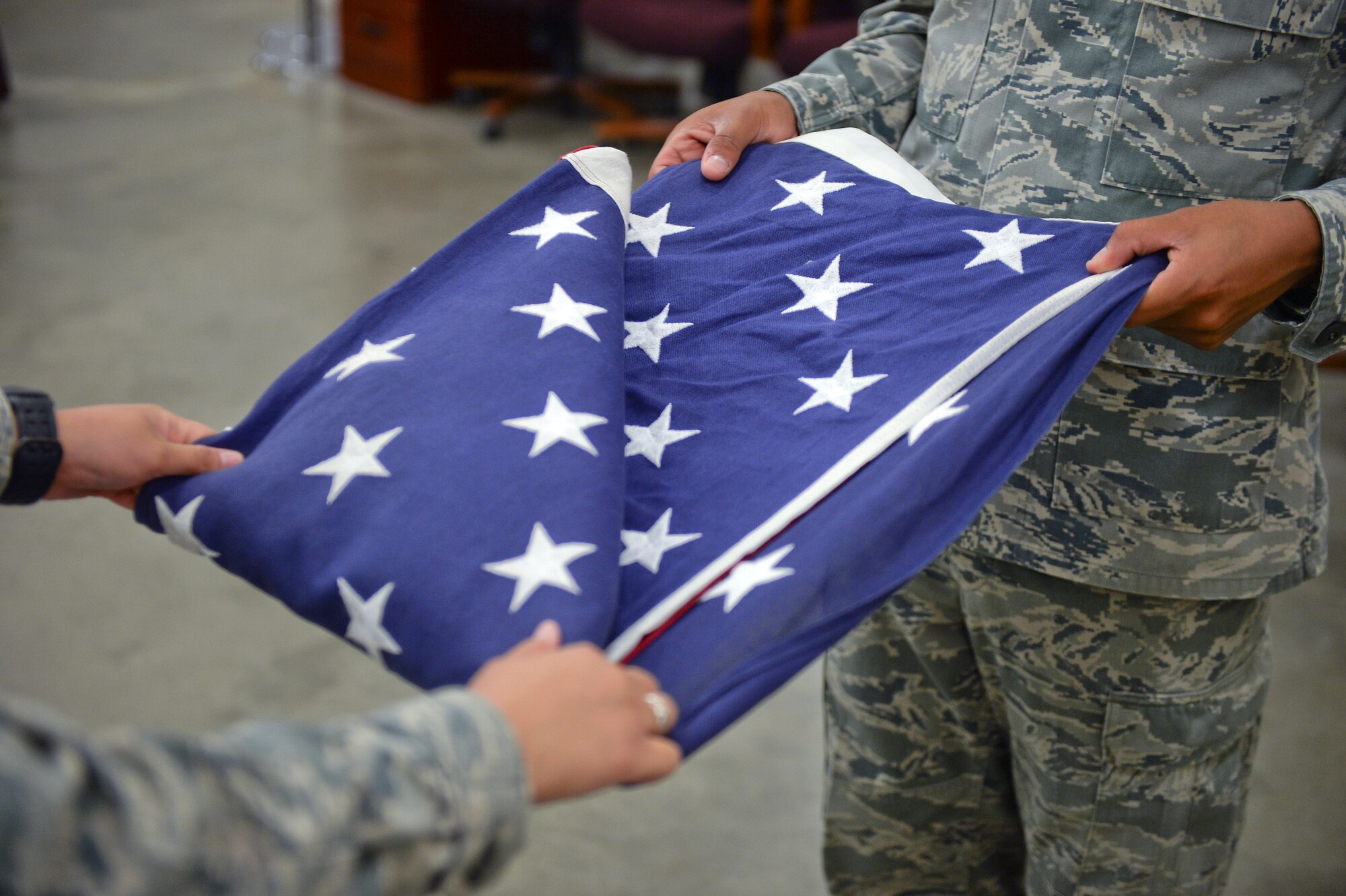 Airman 1st Class Vanessa Manalo, left, and Senior Airman James Cano, 22nd Force Support Squadron honor guardsmen, practice a two-man flag fold July 10, 2015, at McConnell Air Force Base, Kan. The folding and presenting of the flag is part of every full-honors veteran burial service they perform.  (U.S. Air Force photo by Senior Airman Colby L. Hardin)
