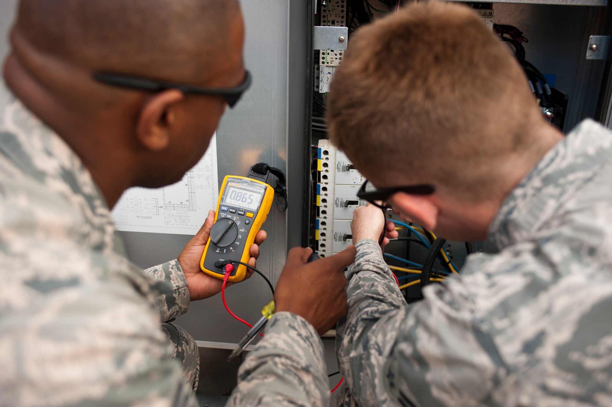 Tech. Sgt. Michael Anderson, left, and Airman 1st Class Zachery Hatfield, both technicians assigned to the 99th Civil Engineer Squadron heating, ventilation, air conditioning and refrigeration shop, check the voltage of a cooling unit at the 99th CES compound on Nellis Air Force Base, Nev., July 7, 2015. Anderson was training Hatfield on how to use and read a meter checking for voltage. (U.S. Air Force photo by Airman 1st Class Mikaley Towle)