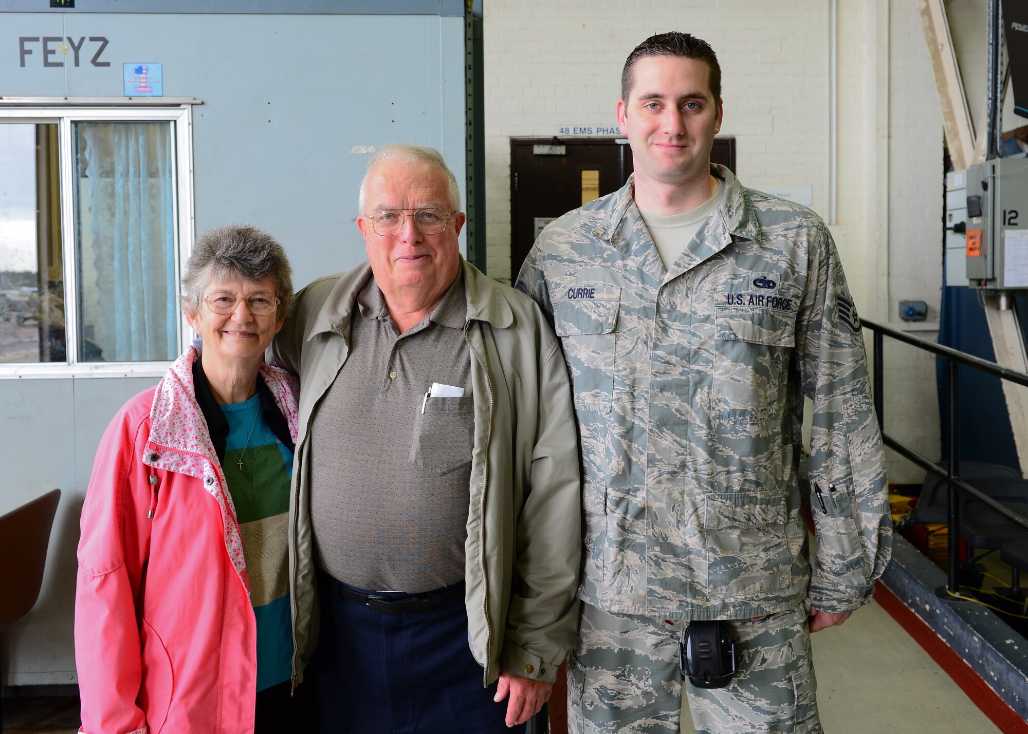 Retired Senior Master Sgt. Robert Fluck, former 48th Equipment Maintenance Squadron aerospace ground equipment craftsman, and wife, Bobbette, pose with Staff Sgt. Justin Currie, 48th  EMS phase inspection team member, during a tour at Hangar 7 at Royal Air Force Lakenheath, July 7, 2015. Fluck’s visit to RAF Lakenheath forged a connection of more than five generations of EMS Airmen. (U.S. Air Force photo by Senior Airman Nigel Sandridge/Released)