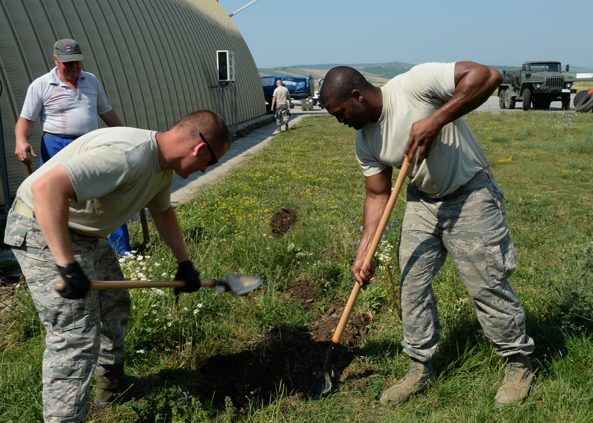 Two U.S. Air Force civil engineer Airmen assigned to the 123rd Expeditionary Fighter Squadron dig a hole to find a waterline alongside a Romanian air force airman on the flightline during a theater security package July 8, 2015, at Campia Turzii, Romania. The Airmen located the waterline to put in a sanitation area for maintainers to use. (U.S. Air Force photo by Senior Airman Dylan Nuckolls/Released)