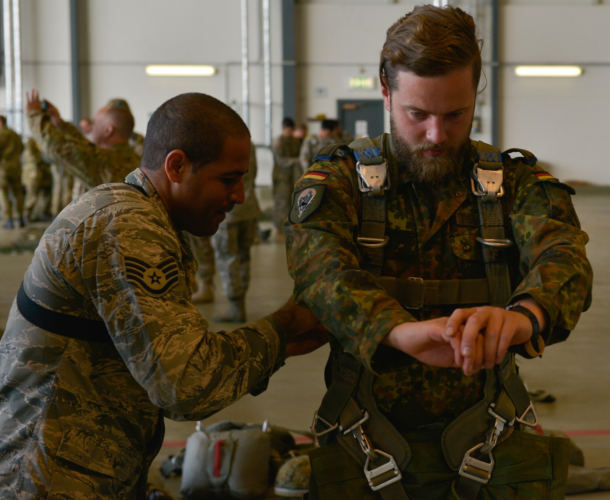 Staff Sgt. Pedro Palmer, 435th Security Forces Squadron contingency response fire team leader, assists a German military member with his harness before loading onto a C-130J Super Hercules July 9, 2015, at Ramstein Air Base, Germany. The 435th Contingency Response Group invited nine allied nations to participate in International Jump Week to boost camaraderie and learn how to work together. (U.S. Air Force photo/Airman 1st Class Lane T. Plummer)