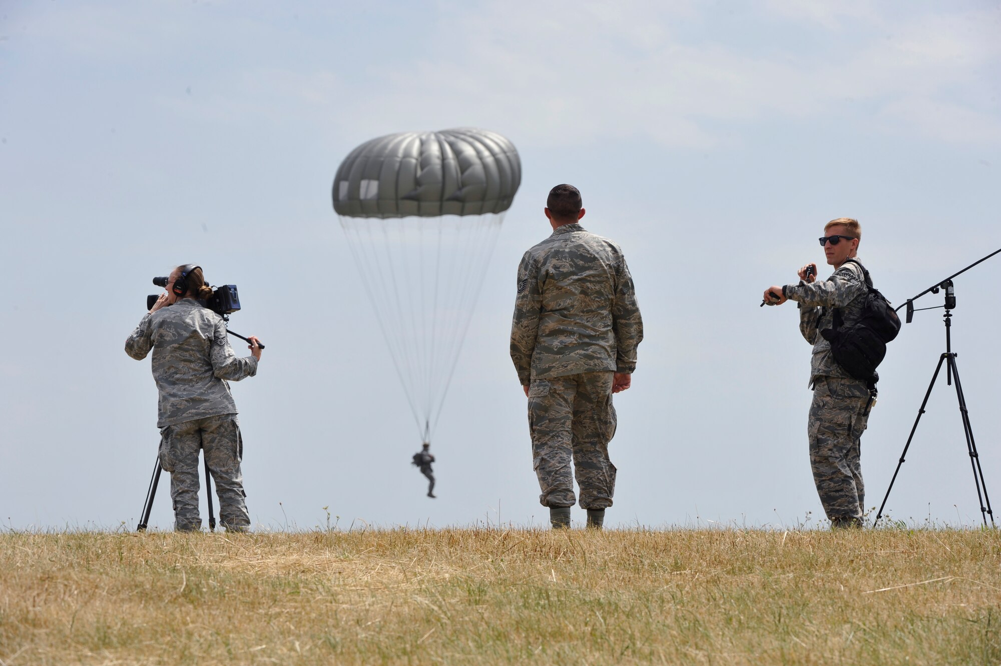 Supporting units watch as paratroopers disembark from a C-130J Super Hercules and land nearby during International Jump Week near Alzey, Germany, July 7, 2015. During jump week, more than 200 U.S. and allied partners exited their designated aircrafts as paratroopers to strengthen and hone procedures and tactics. Supporting units included Air Force and Army medical personnel, air traffic controllers and land navigators. (U.S. Air Force photo/Staff Sgt. Leslie Keopka) 